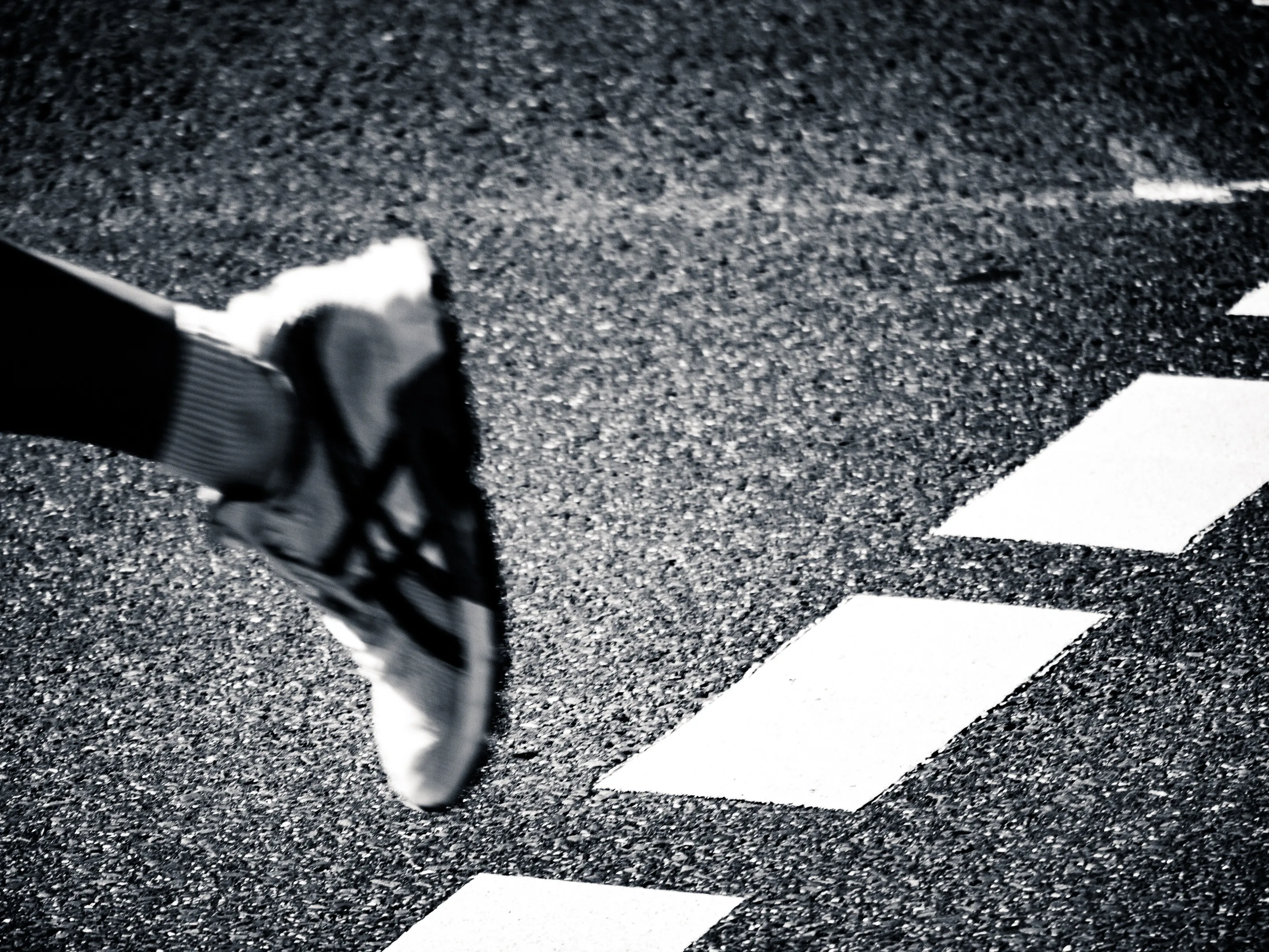 A sneaker stepping on a crosswalk, black and white.