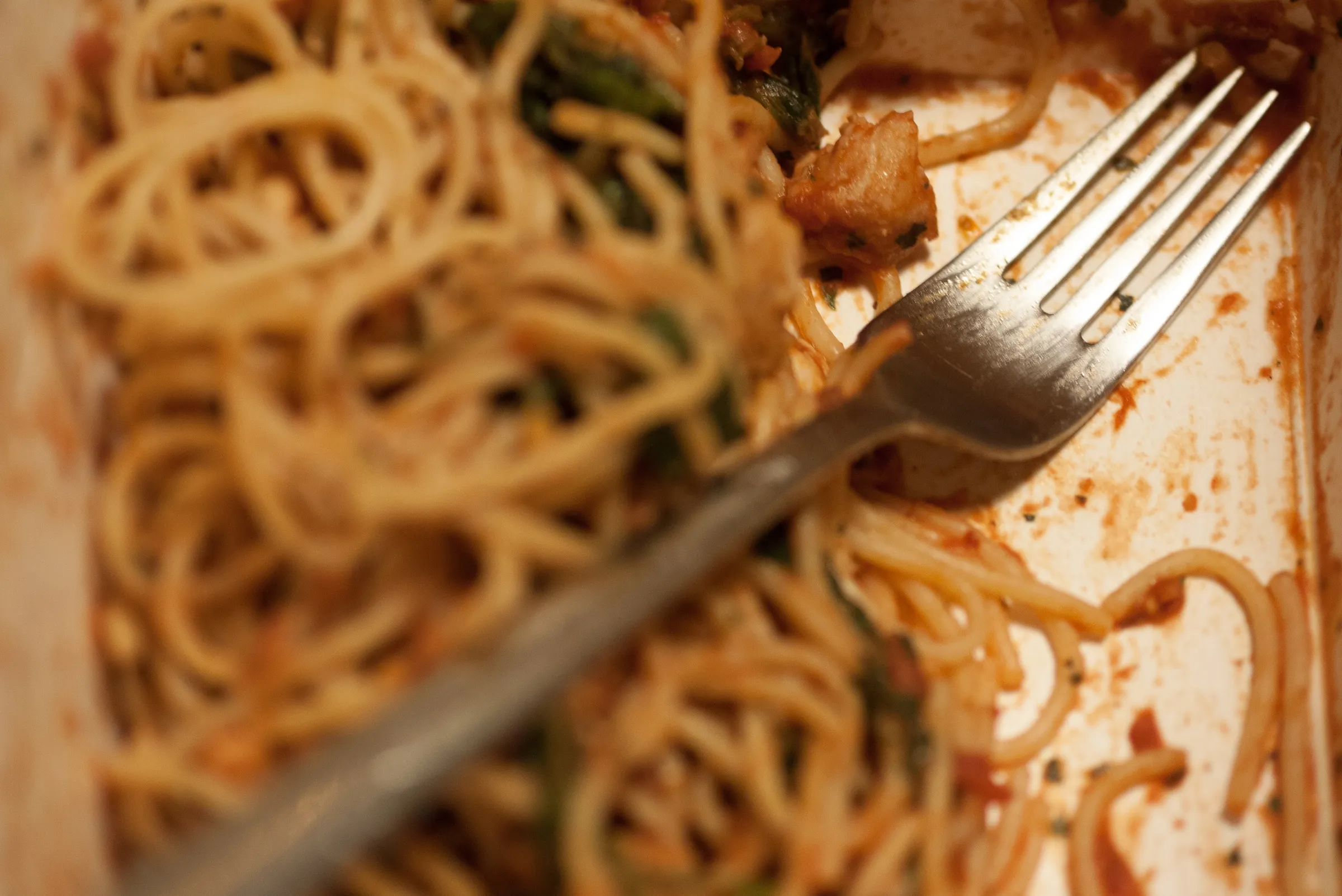 Close-up of spaghetti with tomato sauce and vegetables, fork resting on plate.