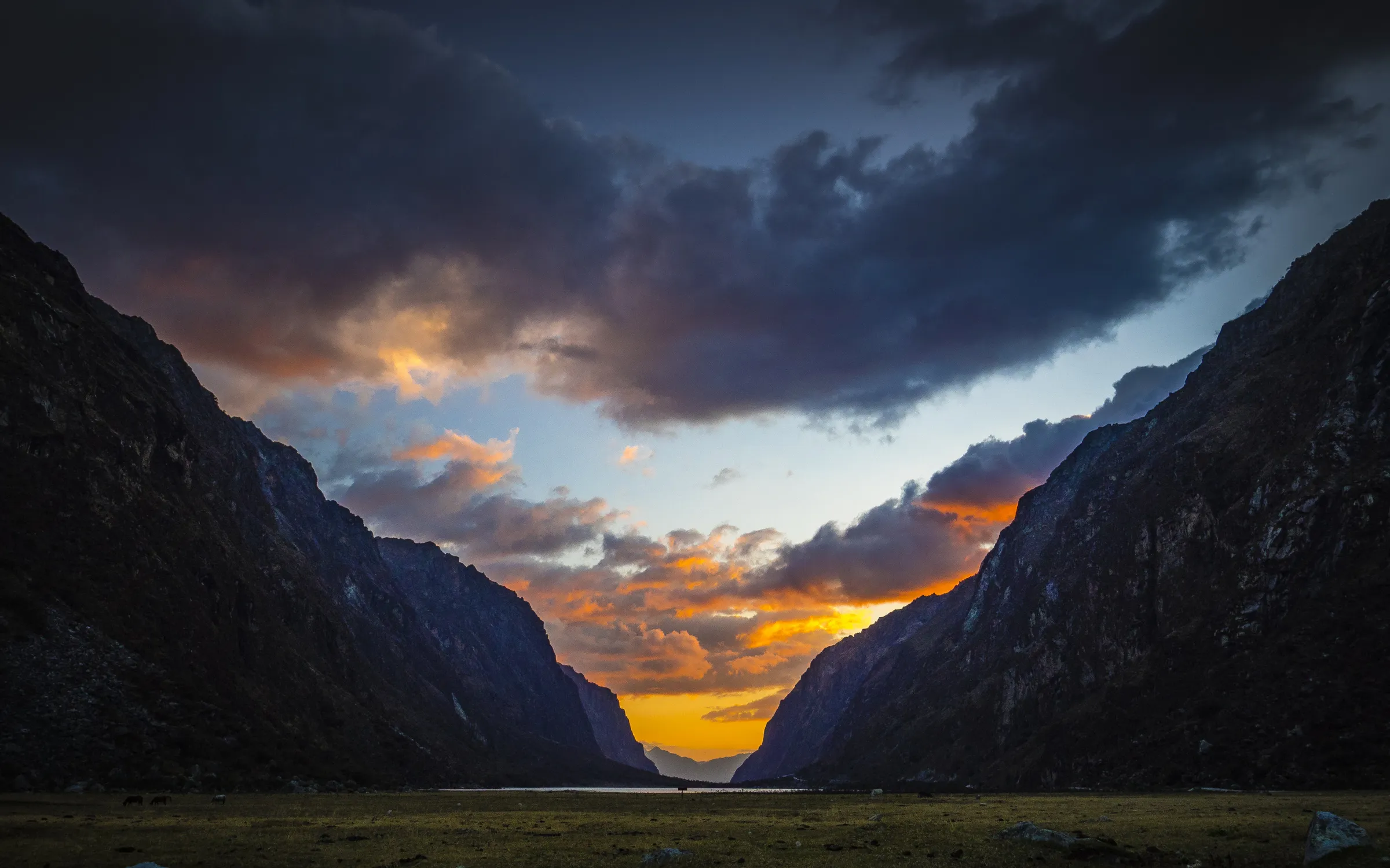 Sunset over mountainous valley, warm colors on clouds, rocky terrain in foreground and shadows.