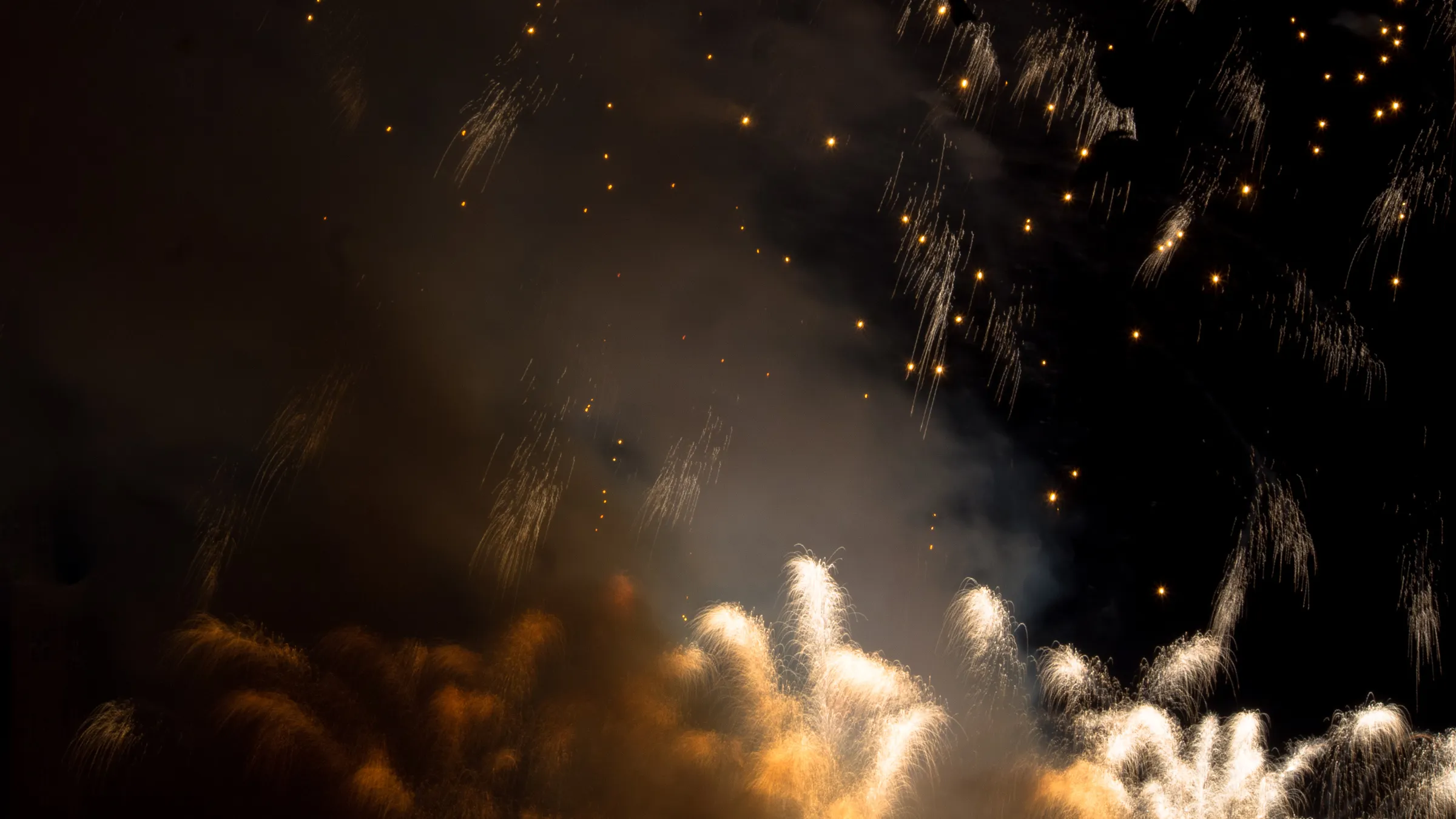 Fireworks bursting in dark sky, golden sparks trailing, bright white explosions at base.