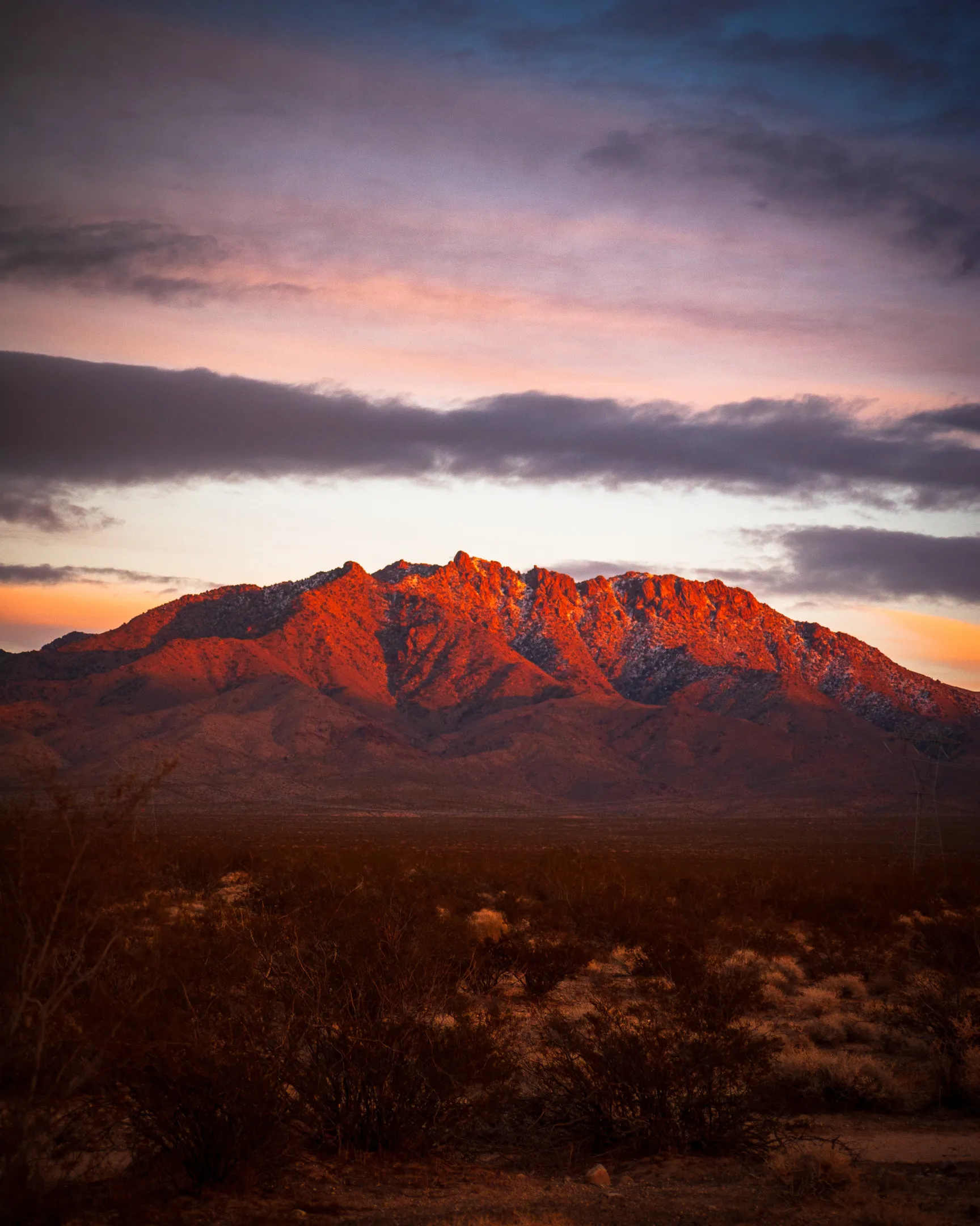 A mountain range at sunset, with pink and orange hues illuminating the peaks against a blue sky.