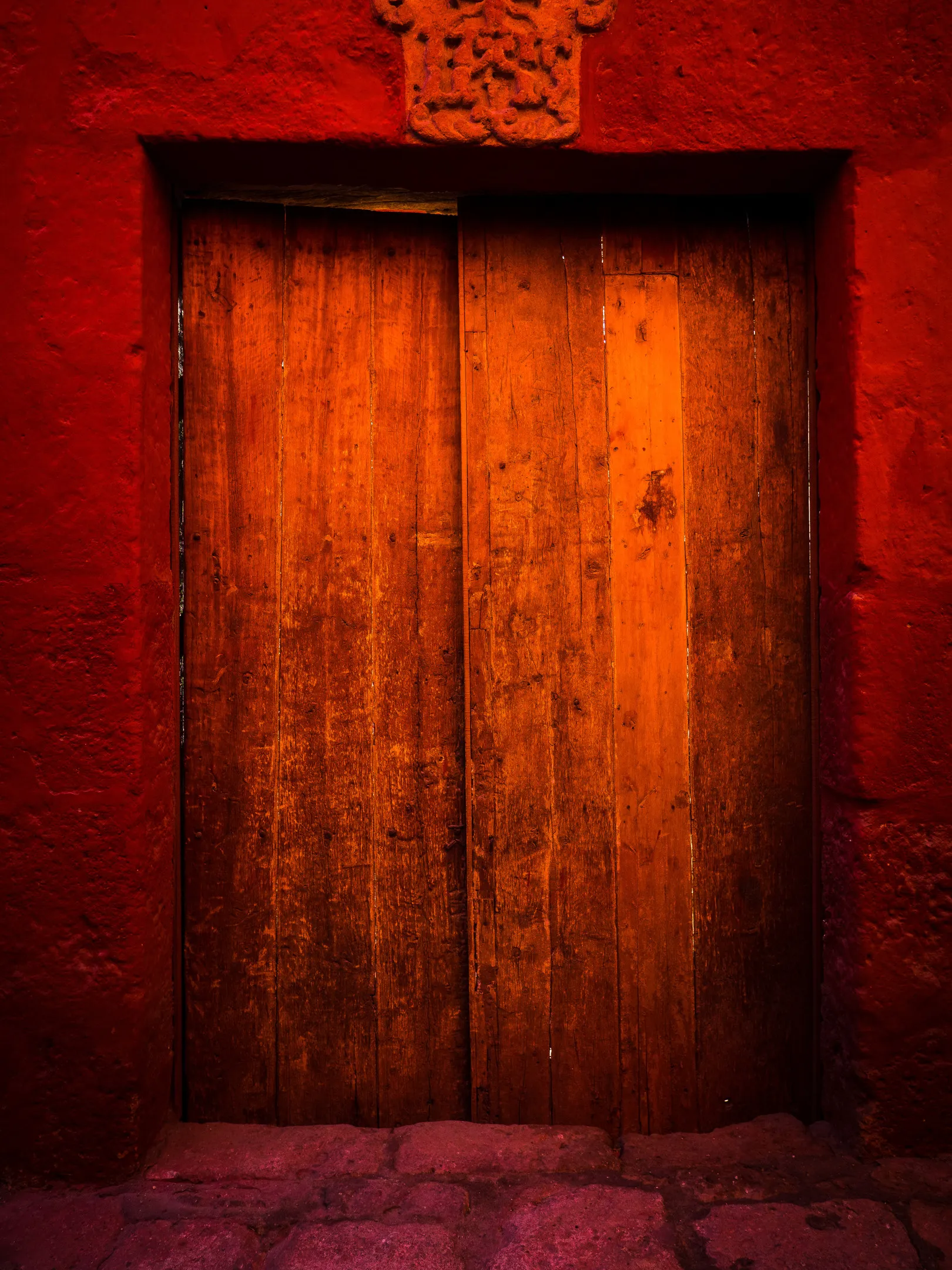 Wooden door in red frame, light streaming from within, textured wall.