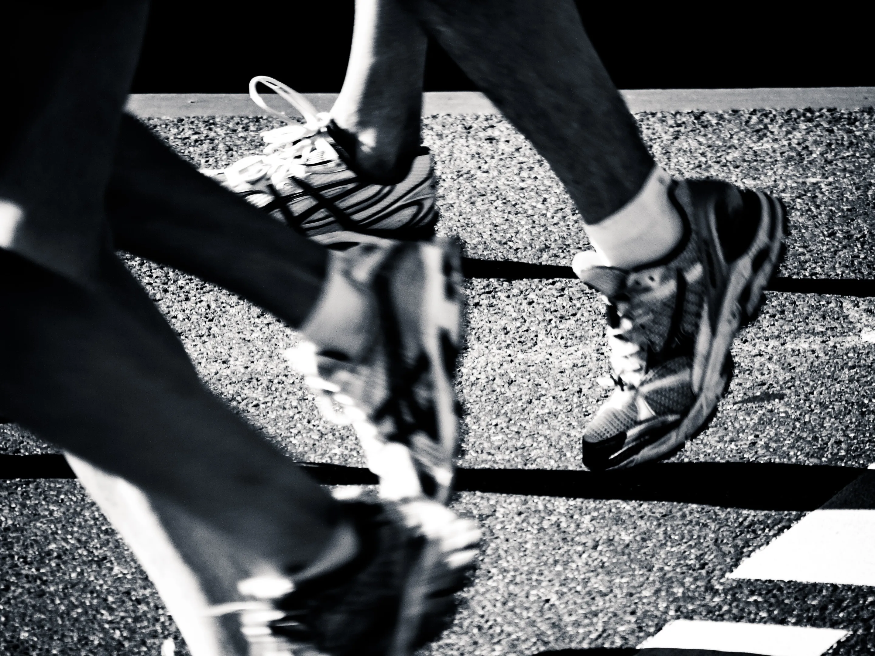 Two people crossing a street, feet in motion on a crosswalk grid.