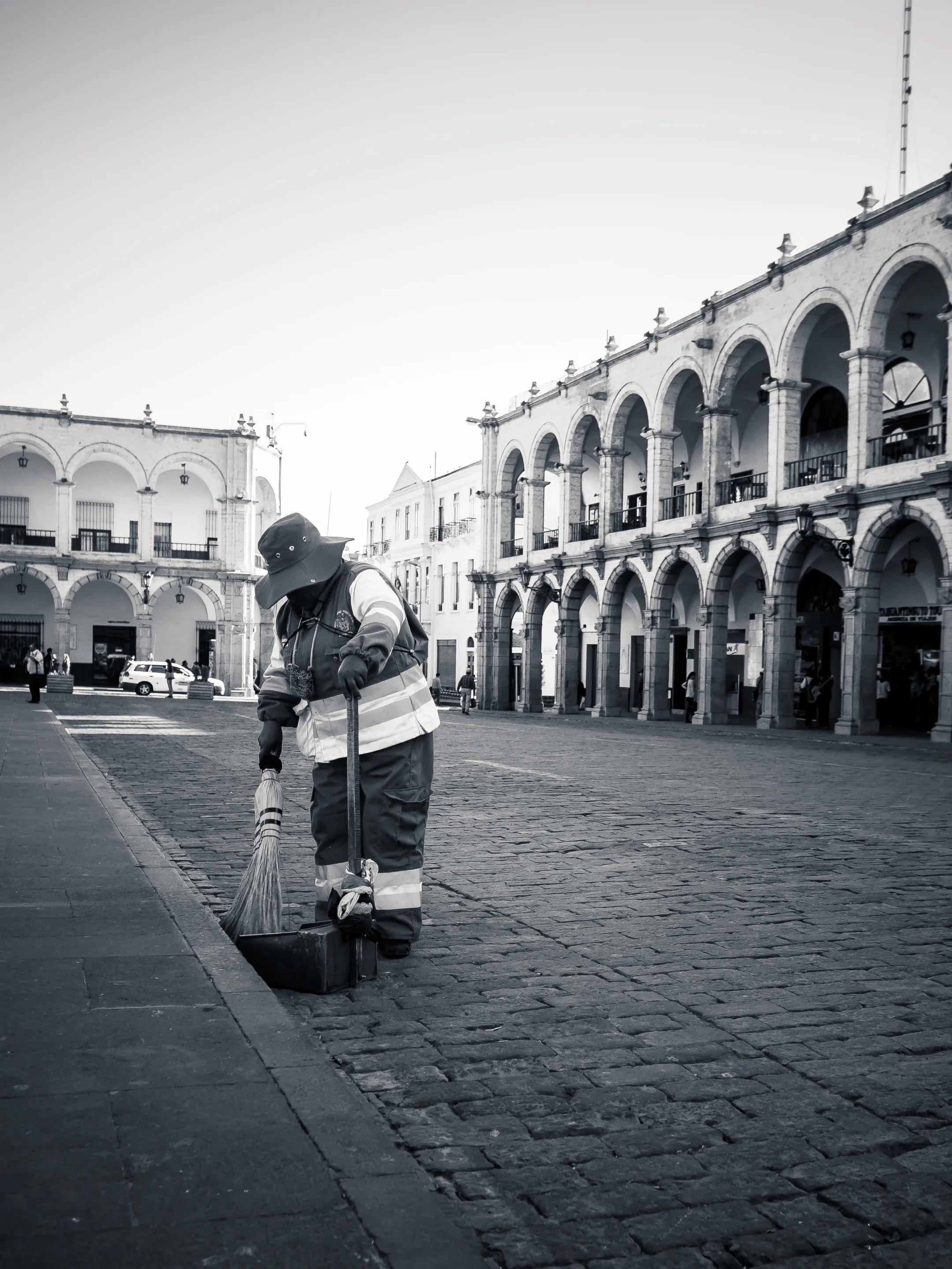 A worker sweeping the street in front of an ornate building with arches and balconies.