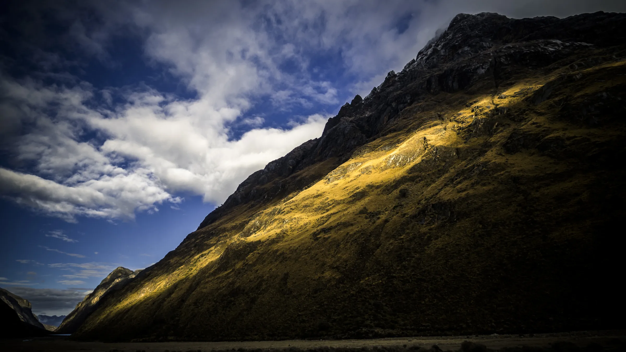 Mountain slope bathed in golden sunlight under a blue sky with scattered clouds.