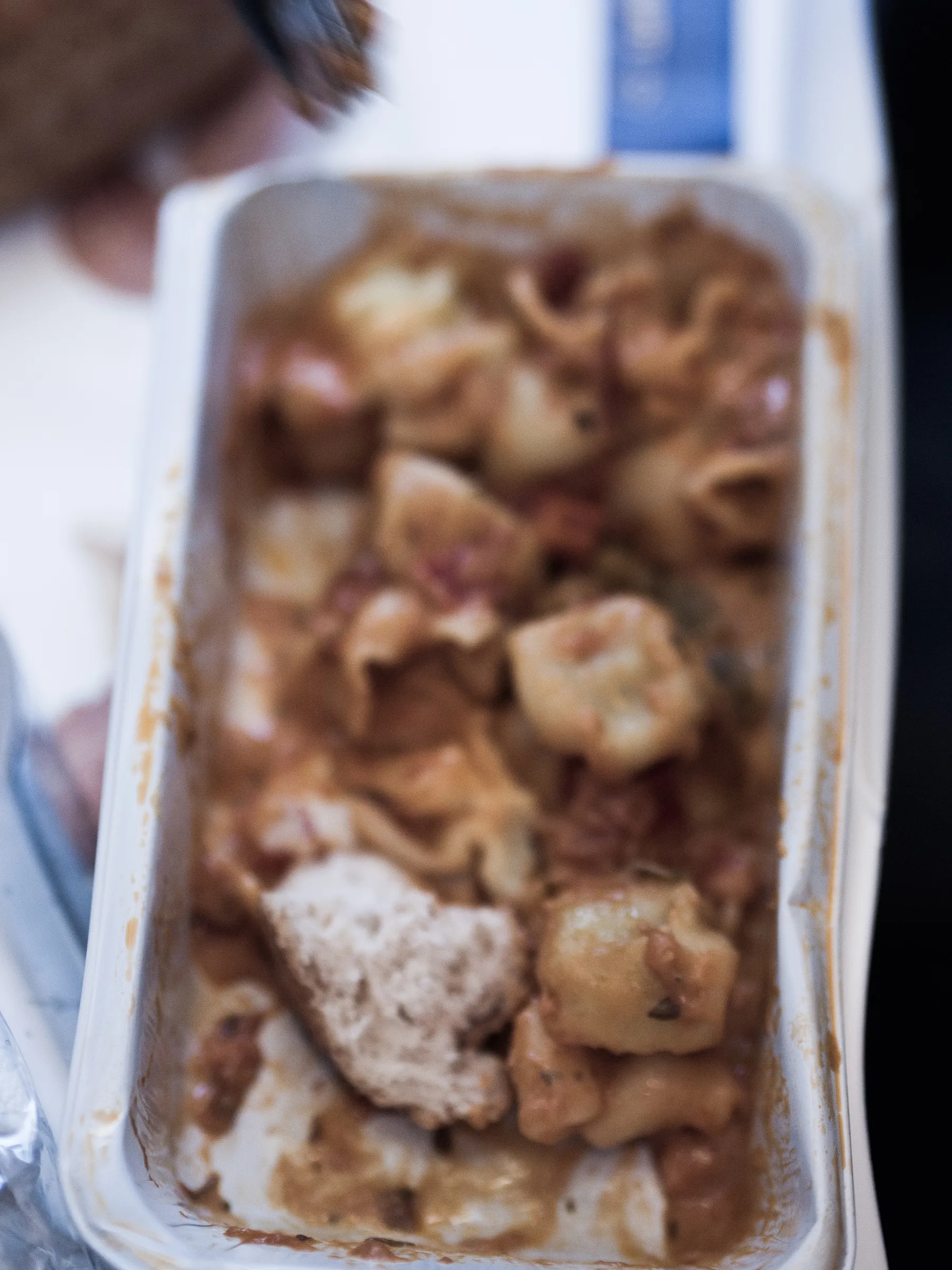 Pasta dish in a white takeout container, topped with creamy sauce and visible chunks of chicken.