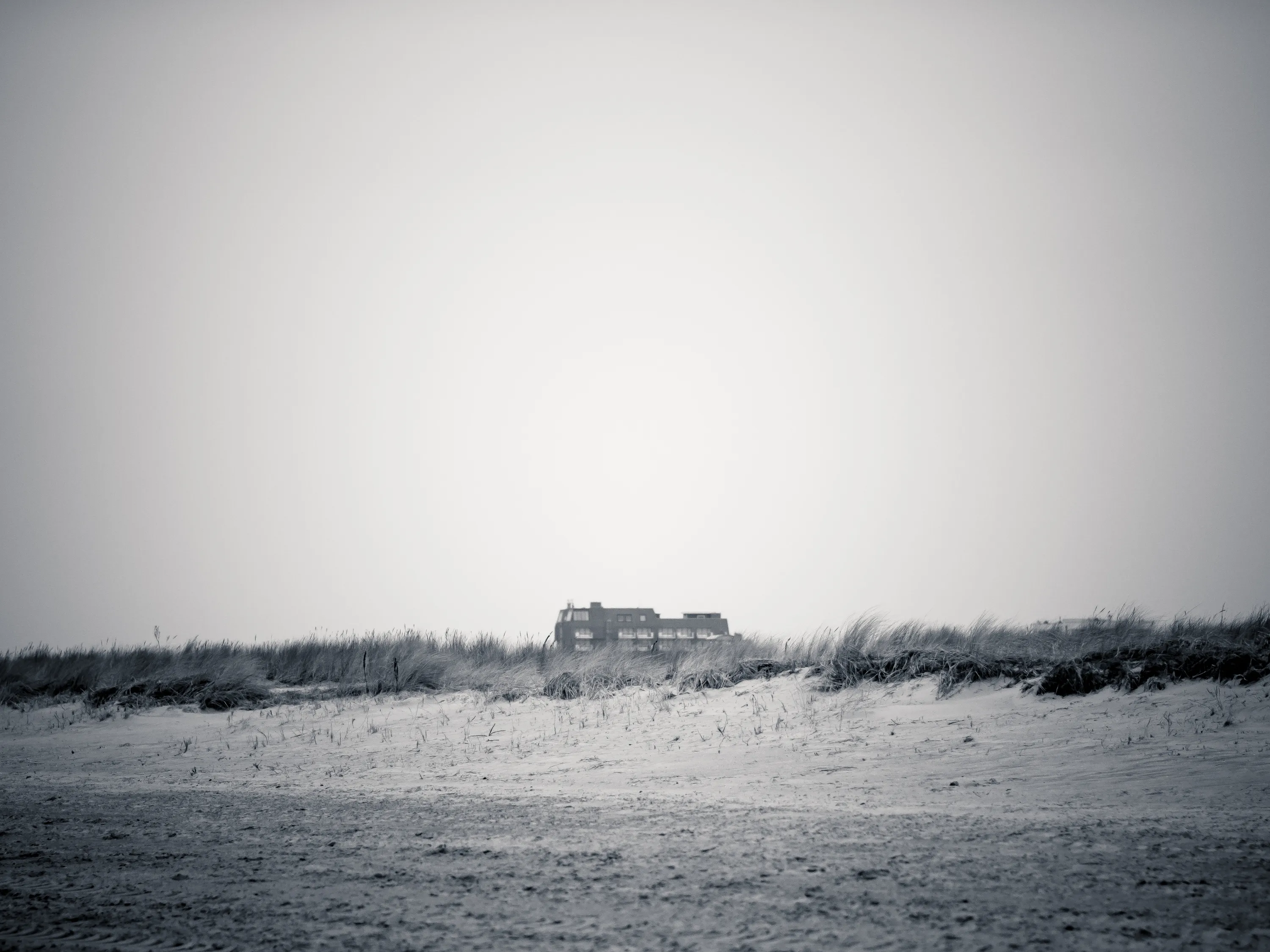 Black and white beach scene with lone house in distance, dunes in foreground.