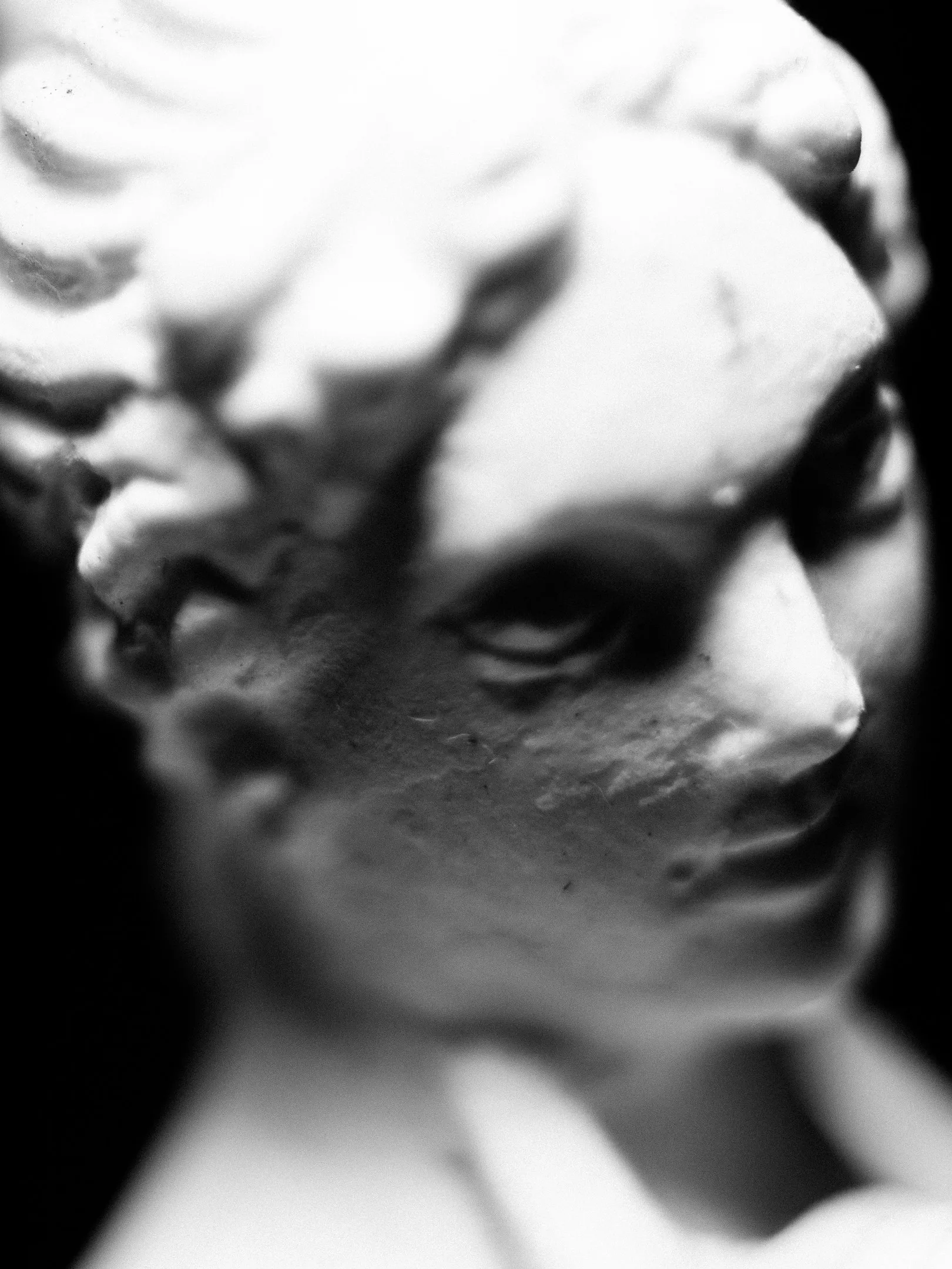 Close-up of a weathered statue's face, capturing details in monochrome.