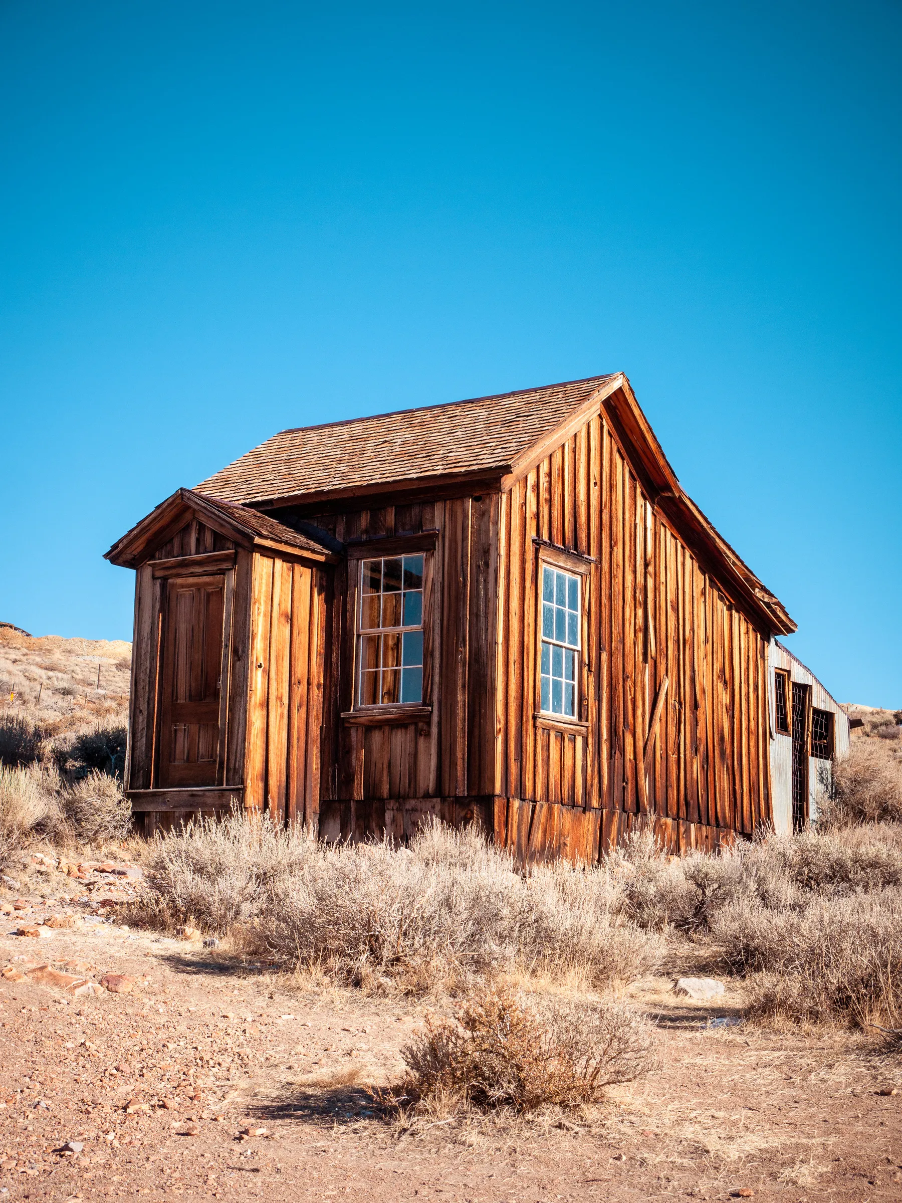 Weathered wooden cabin with a single window, set in arid landscape with dry grass.