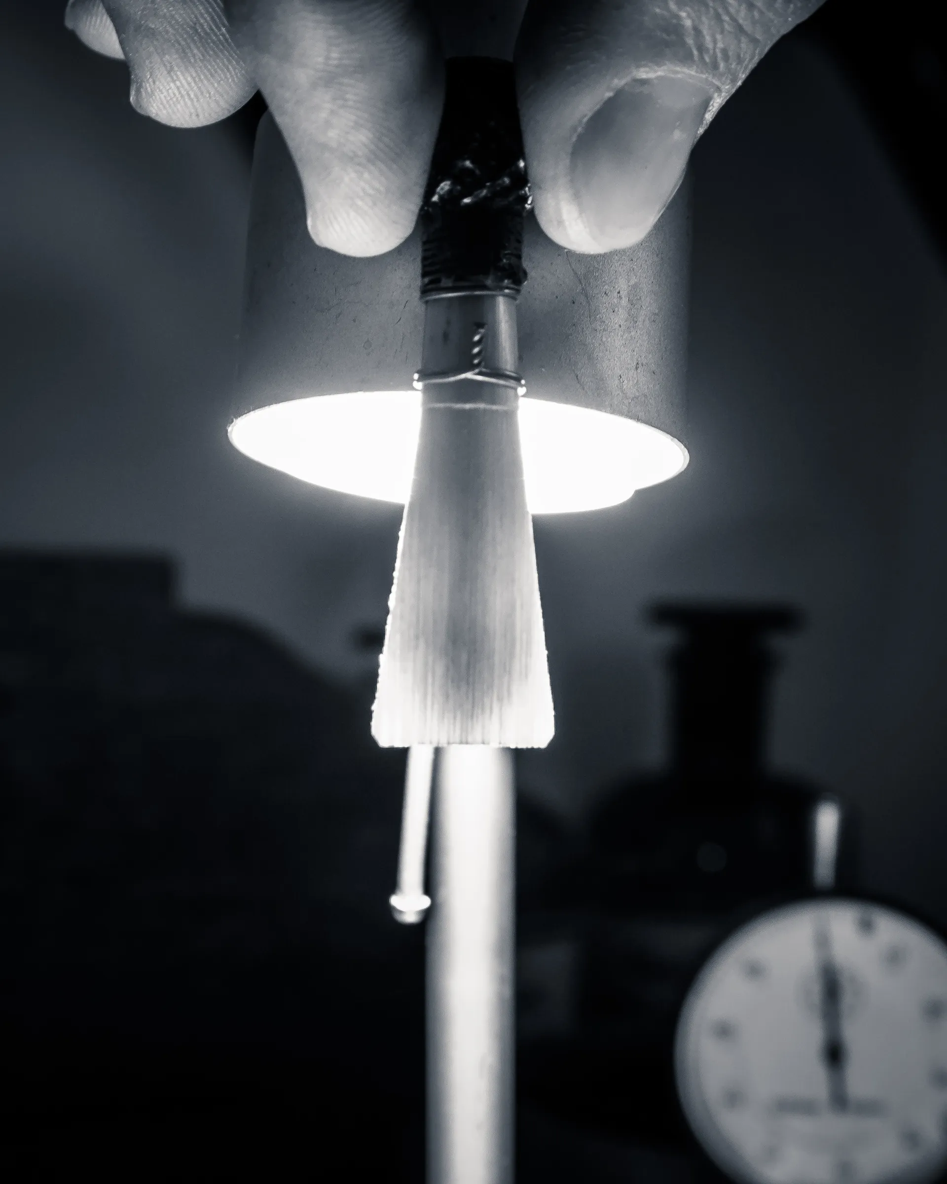 Hand adjusting a desk lamp with a white lampshade, casting light on a blurred clock face in the background.