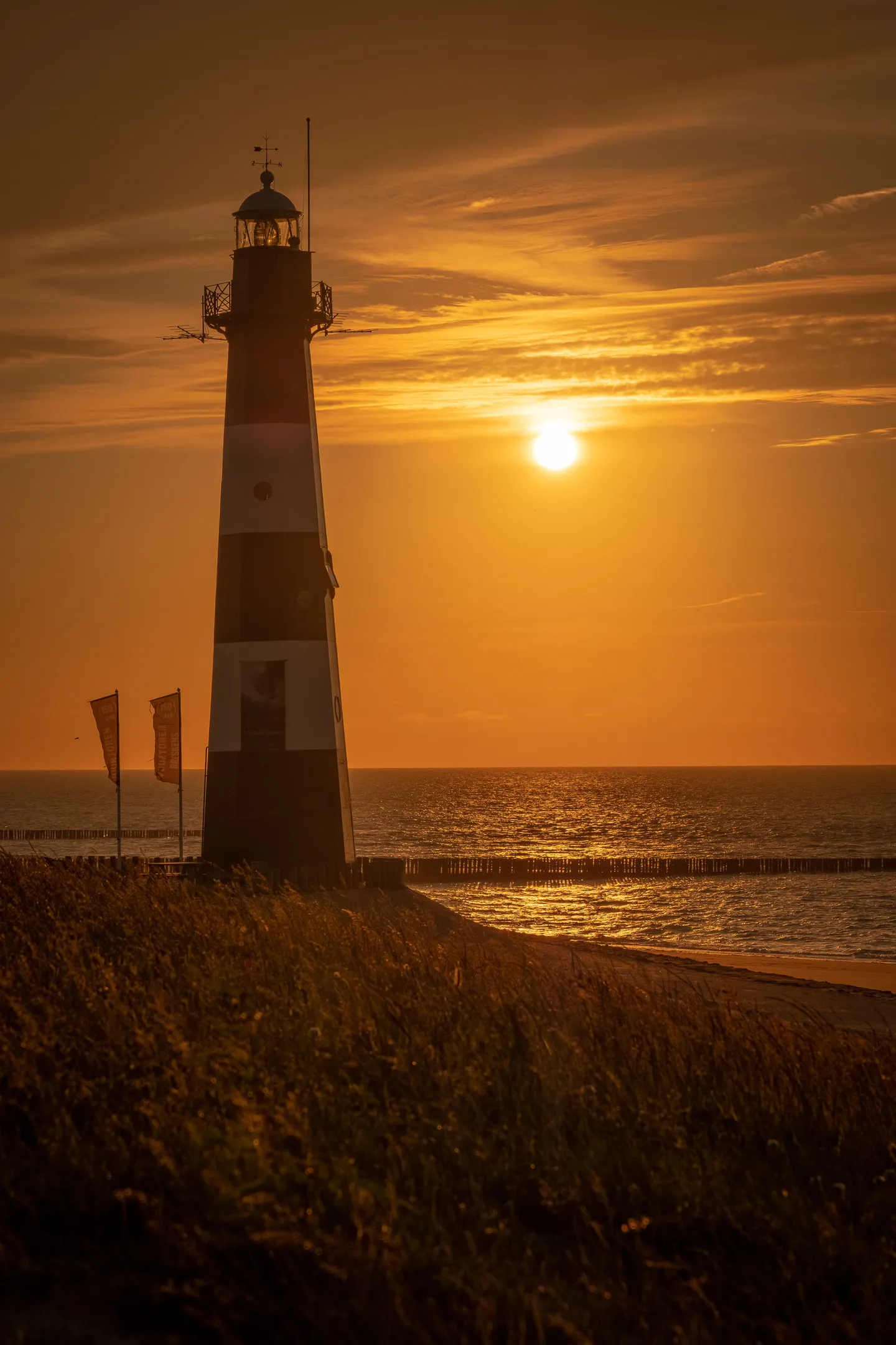 Lighthouse silhouette at sunset, overlooking a grassy shore and calm sea.