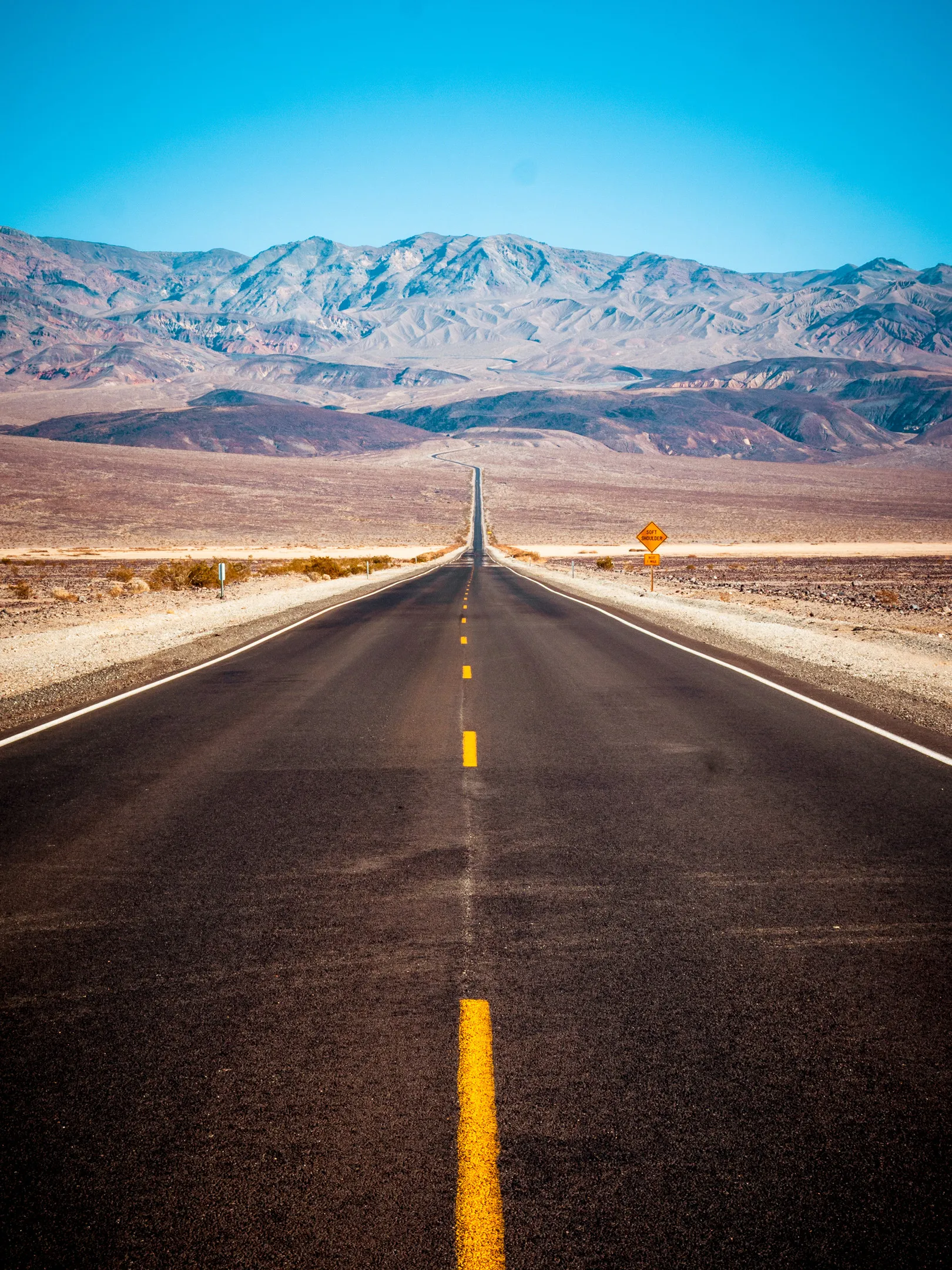 A long, straight road stretching towards mountains in a vast desert landscape.