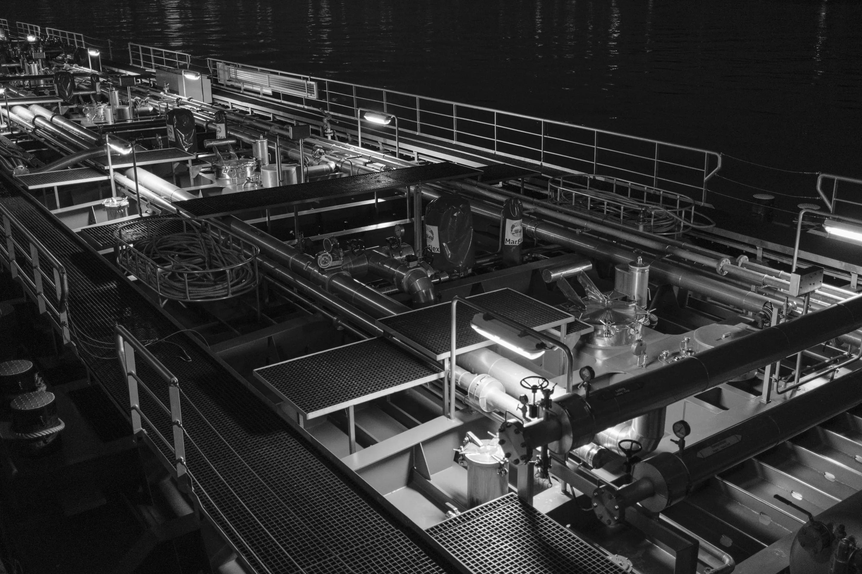 Industrial ship deck with complex machinery and equipment at night, illuminated by artificial lights.