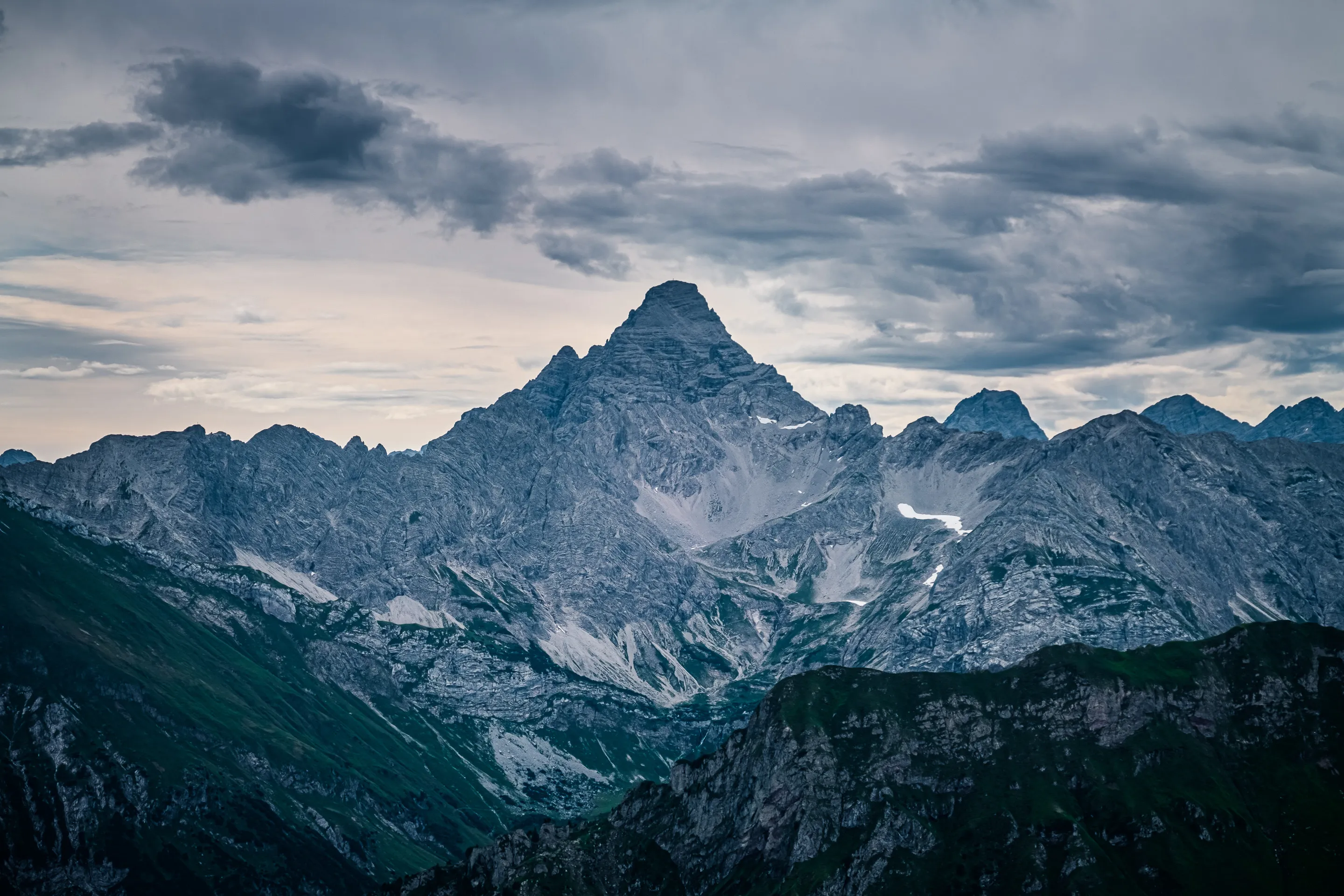 Majestic mountain peak under a cloudy sky, with rugged slopes and patches of snow.