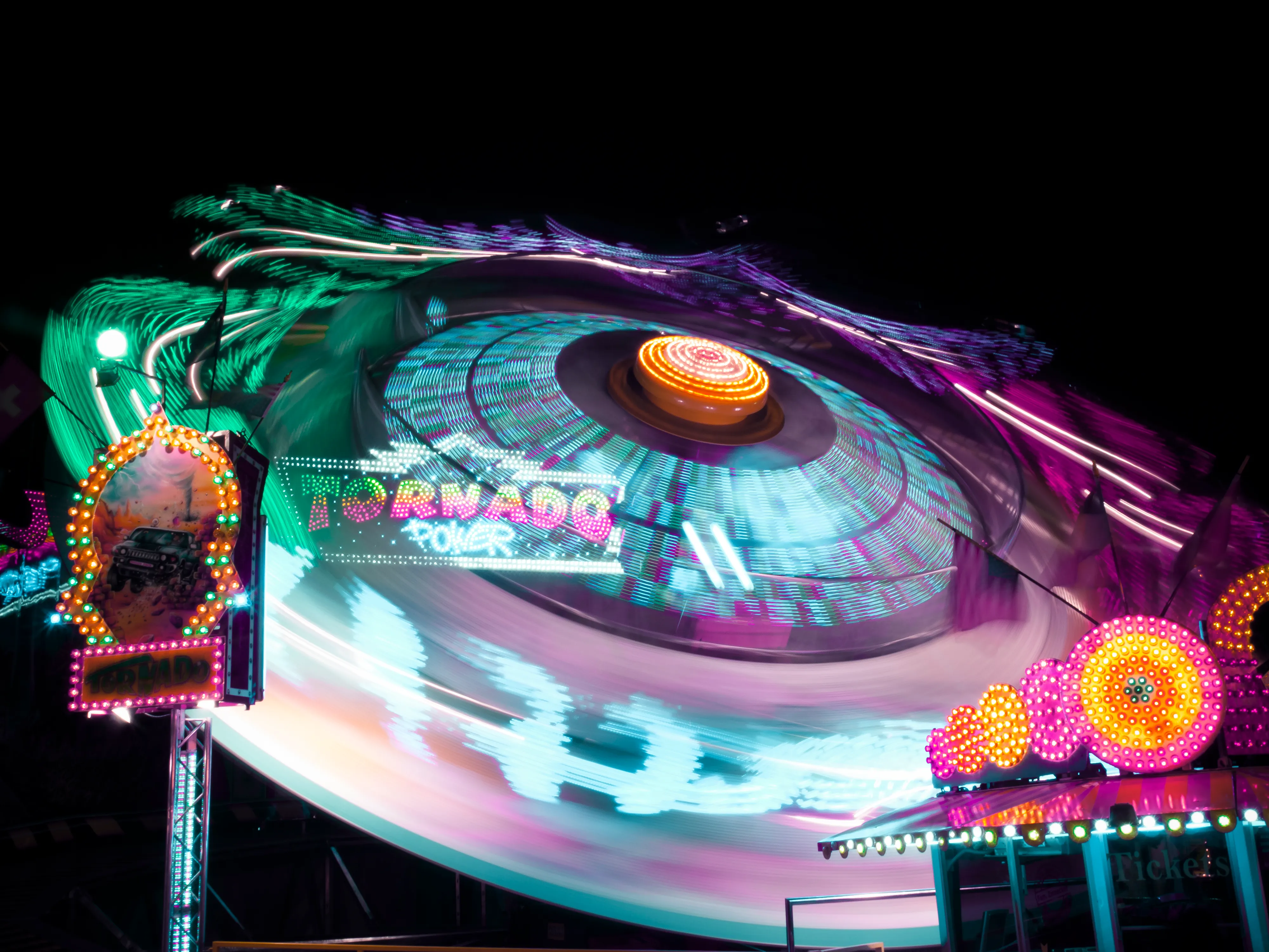 A vibrant carnival ride, Tornado, spinning at night with colorful lights, a dragon head at the top, and blurred motion from its rotation.