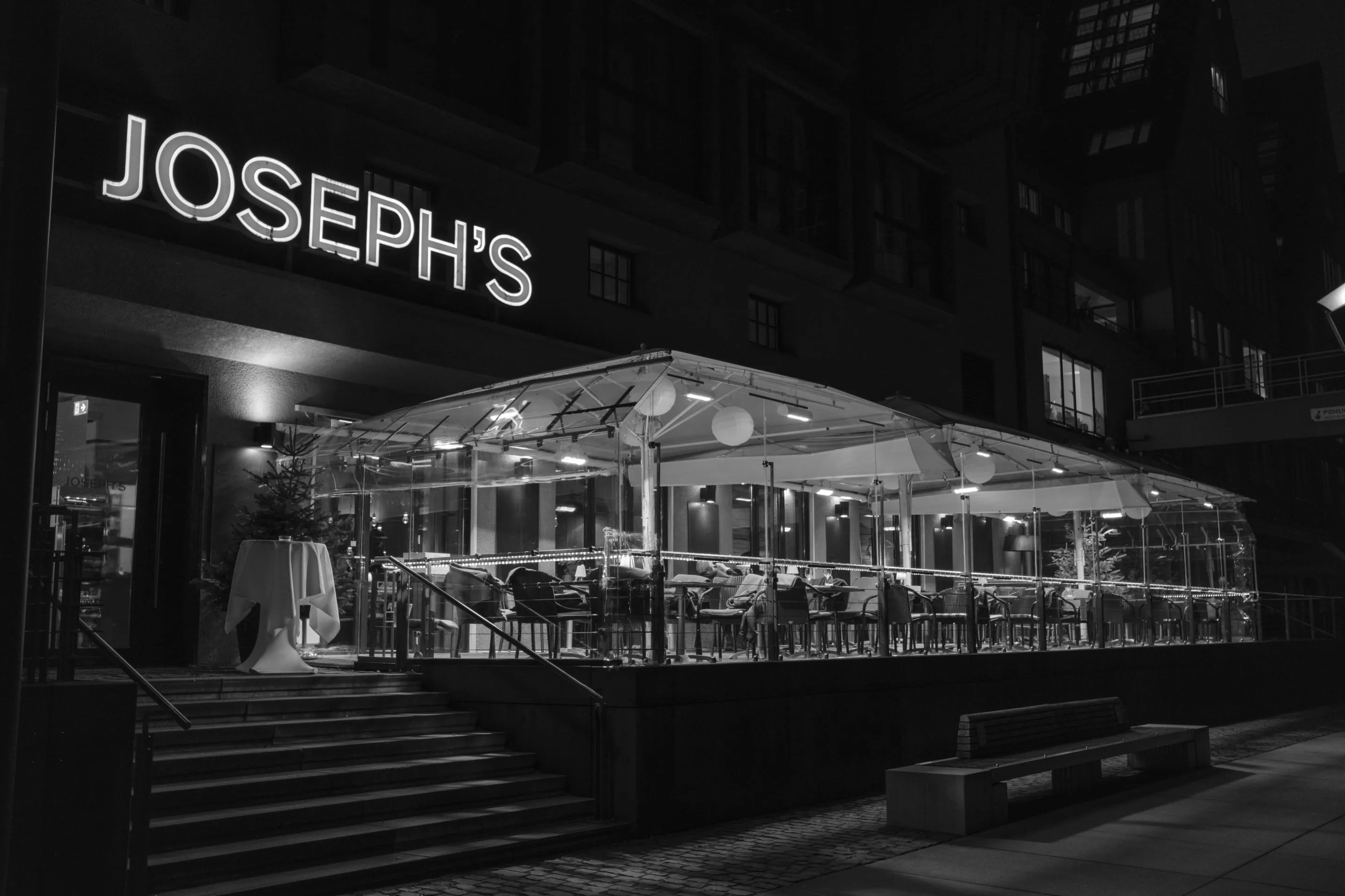 Night view of Joseph's restaurant with outdoor seating under umbrellas, lit up against a dark building facade.