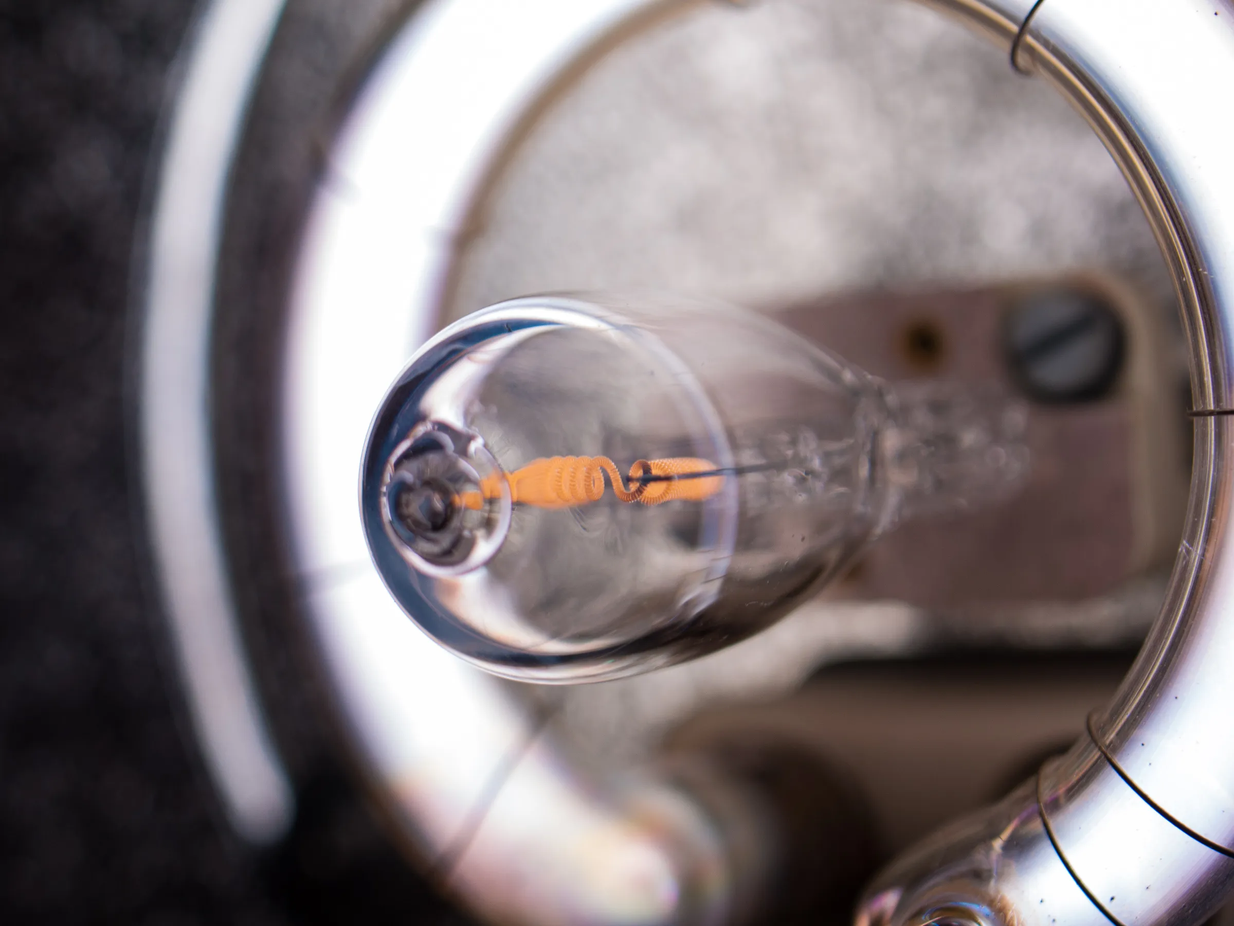 Close-up of a lightbulb with a visible glowing filament, encased in clear glass, against a blurred background.