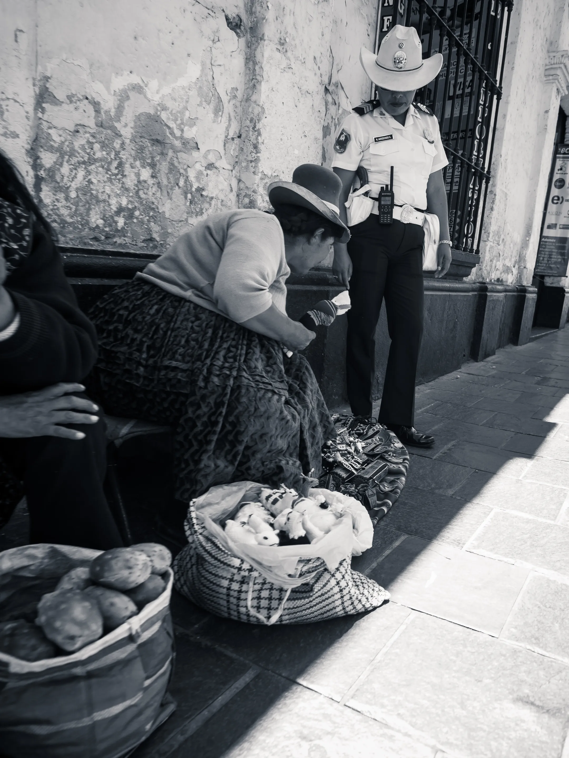 Woman selling potatoes from a basket, cowboy hat man standing with police officer on street.