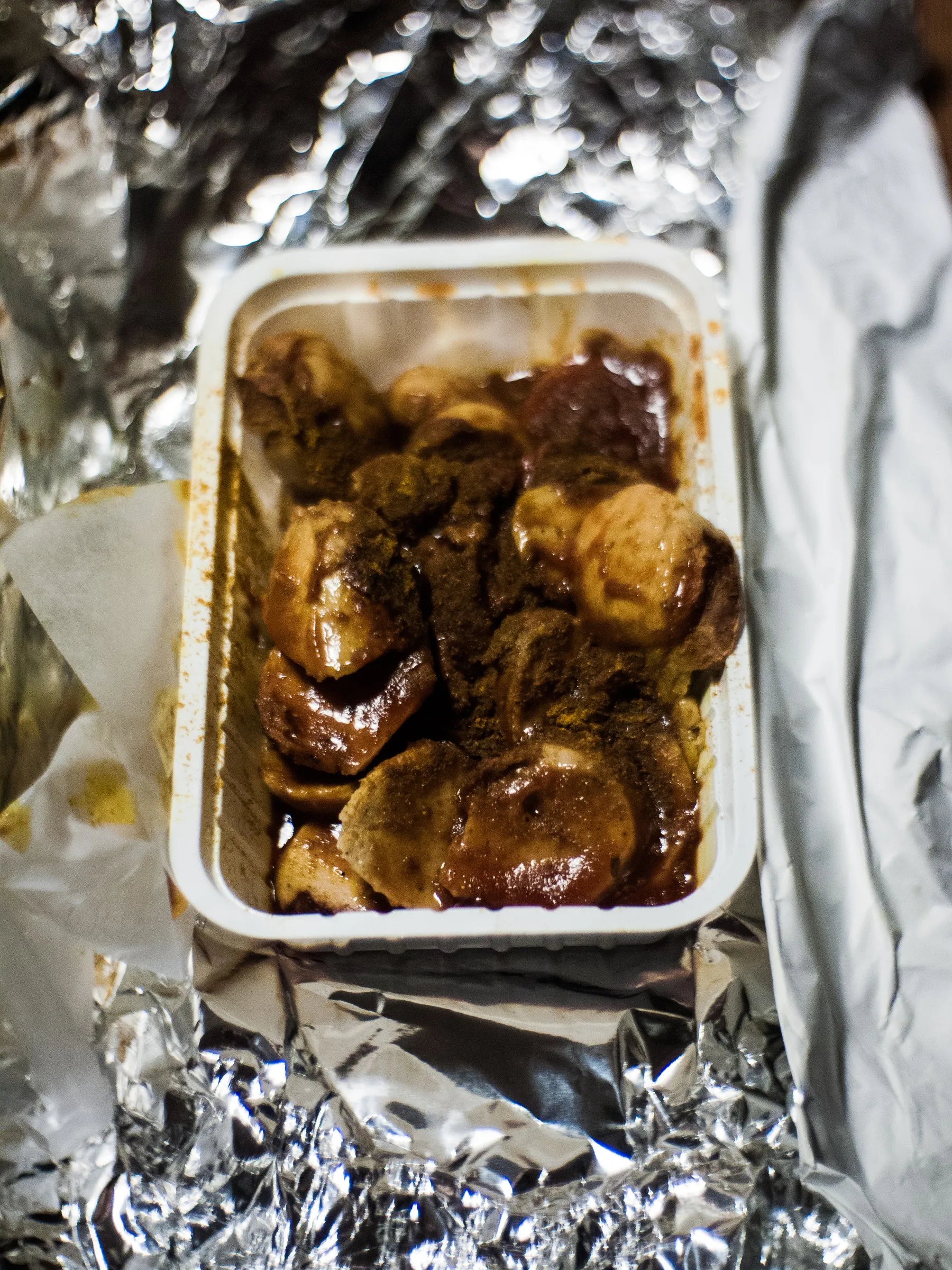 A takeout container with roasted meat, foil, and napkin underneath.