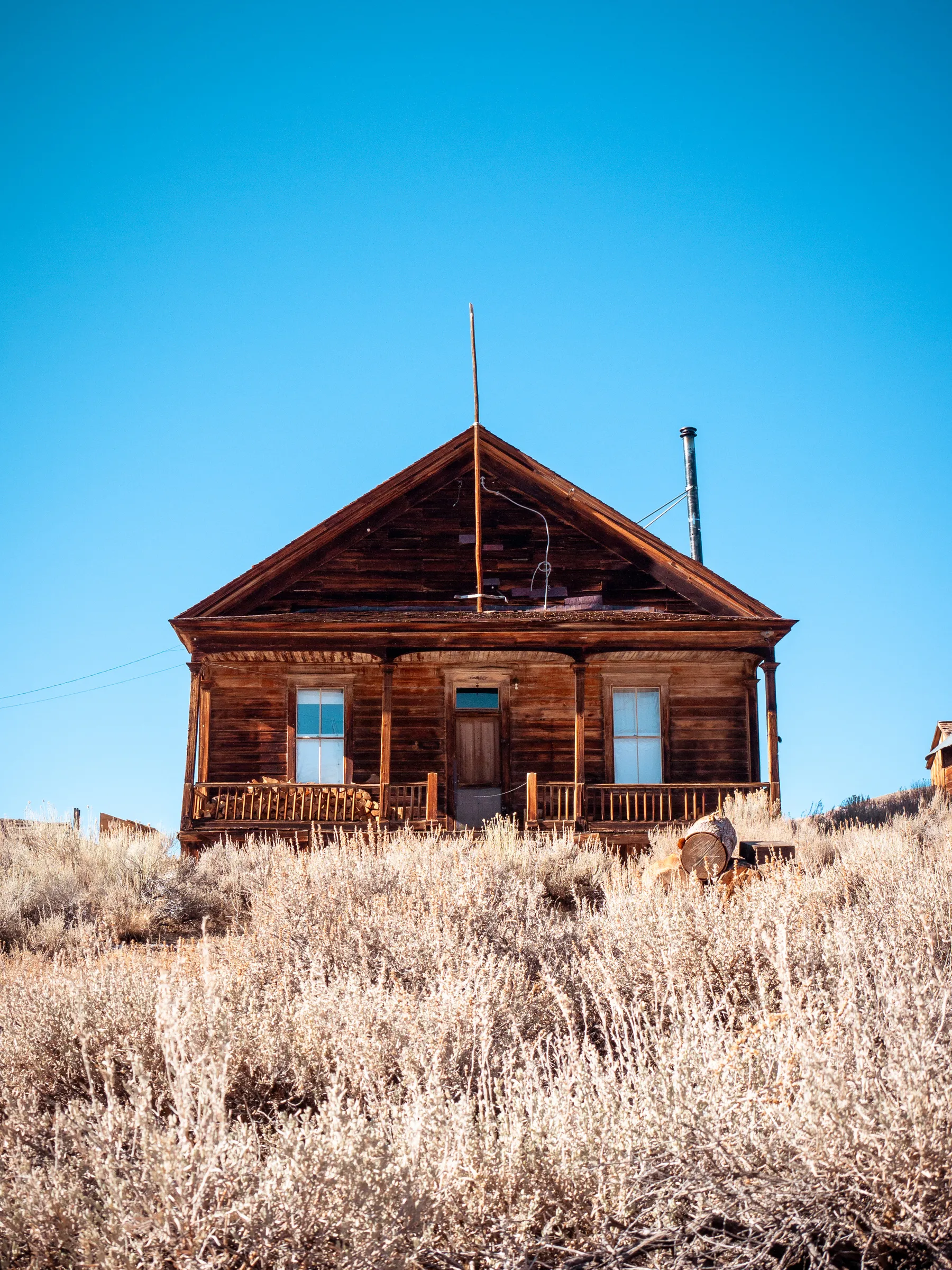Weathered wooden house with a porch, surrounded by dry grass, clear blue sky.