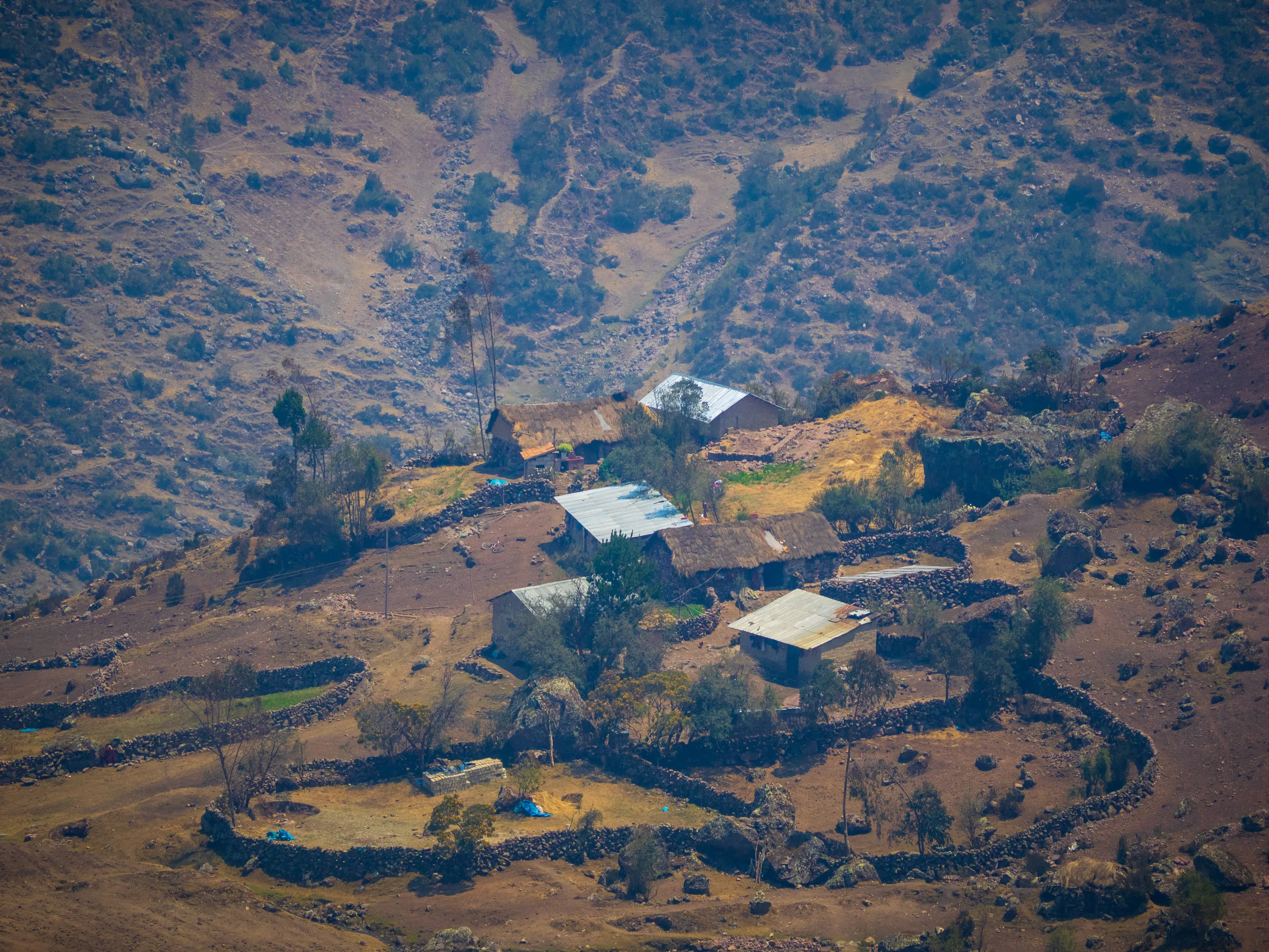 Hillside village with scattered houses, surrounded by arid landscape and sparse vegetation.