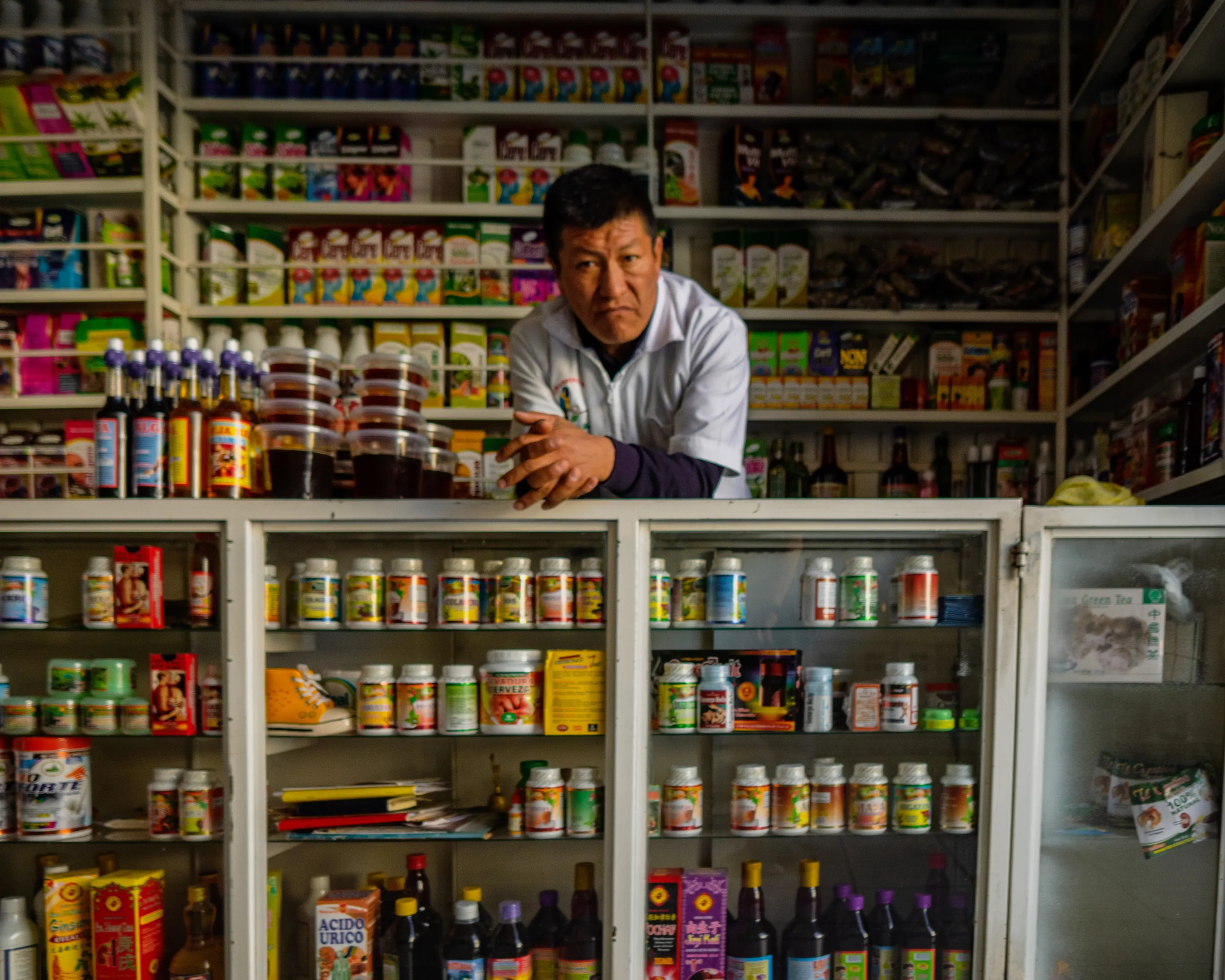 A man in a white shirt standing behind shelves filled with various jars, bottles, and boxes of colorful products in a store.