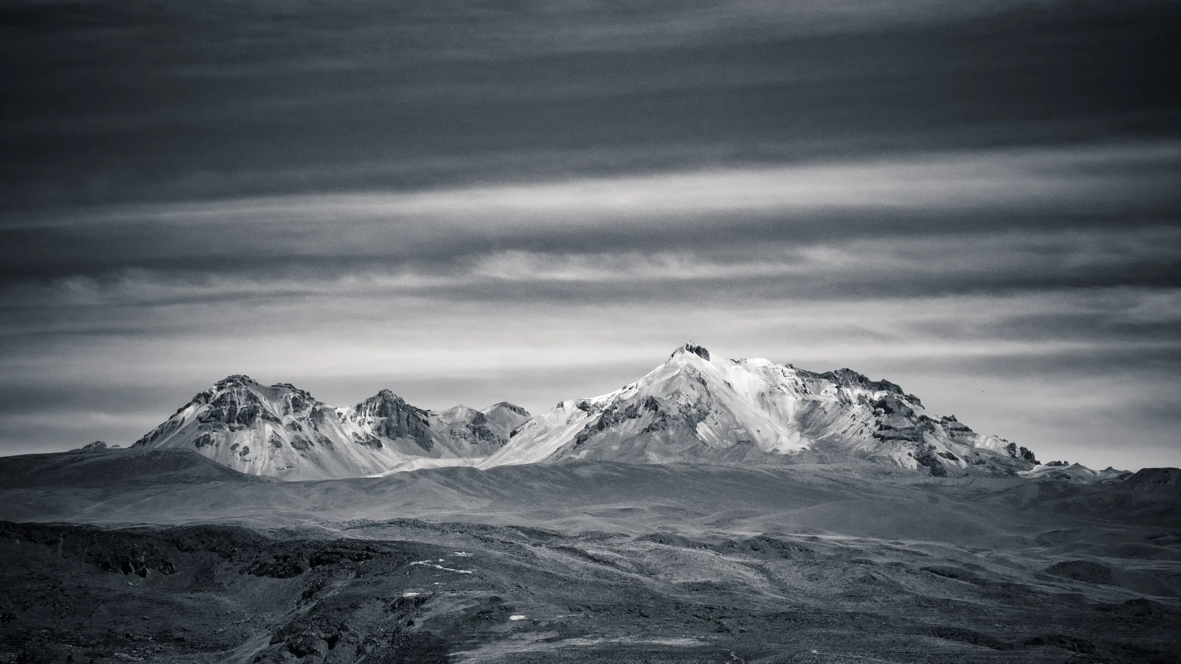 Mountain range with snow-capped peaks under a cloudy sky, black and white.
