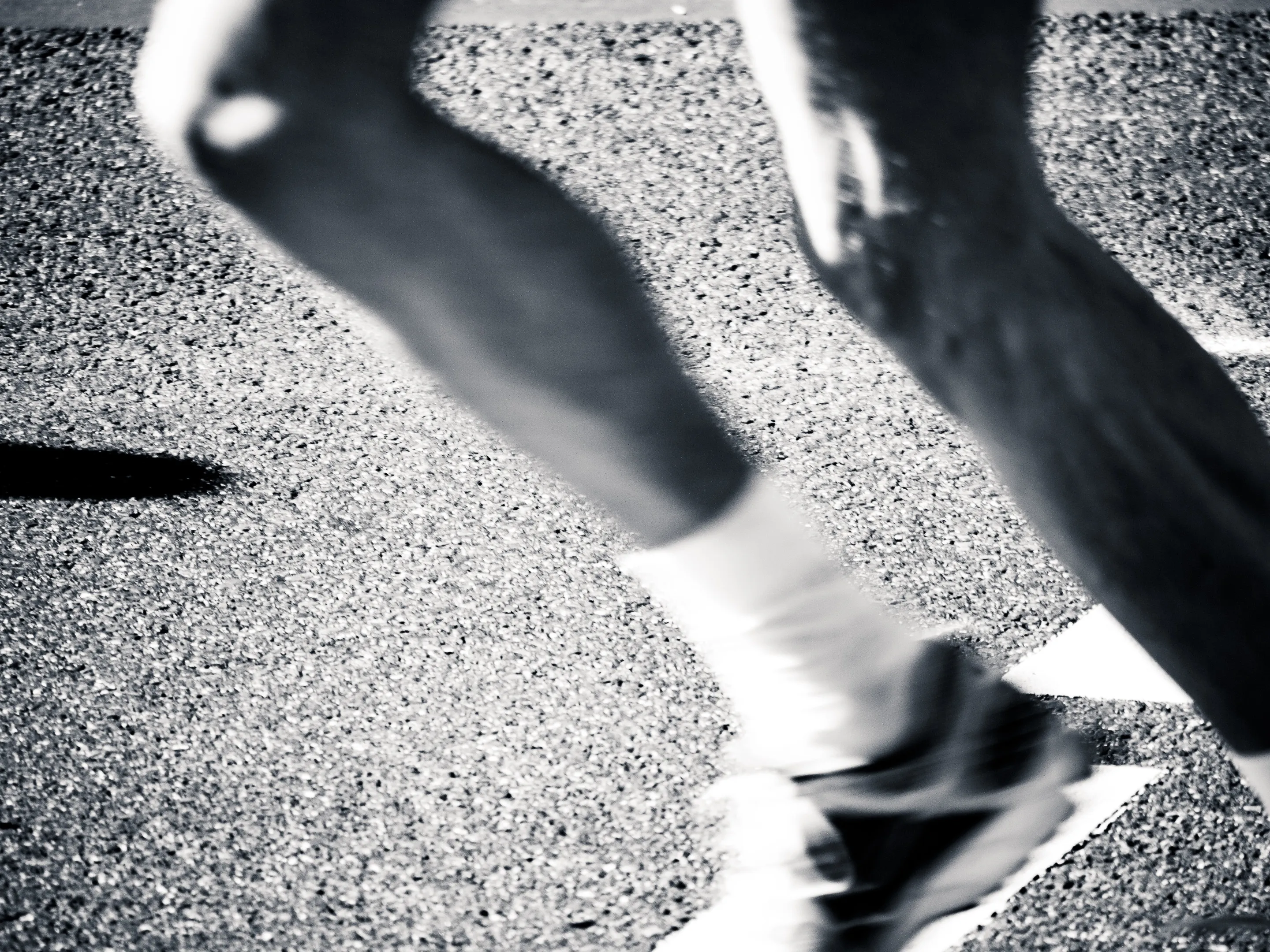 Close-up of feet in motion on a pebbly surface, captured in black and white.