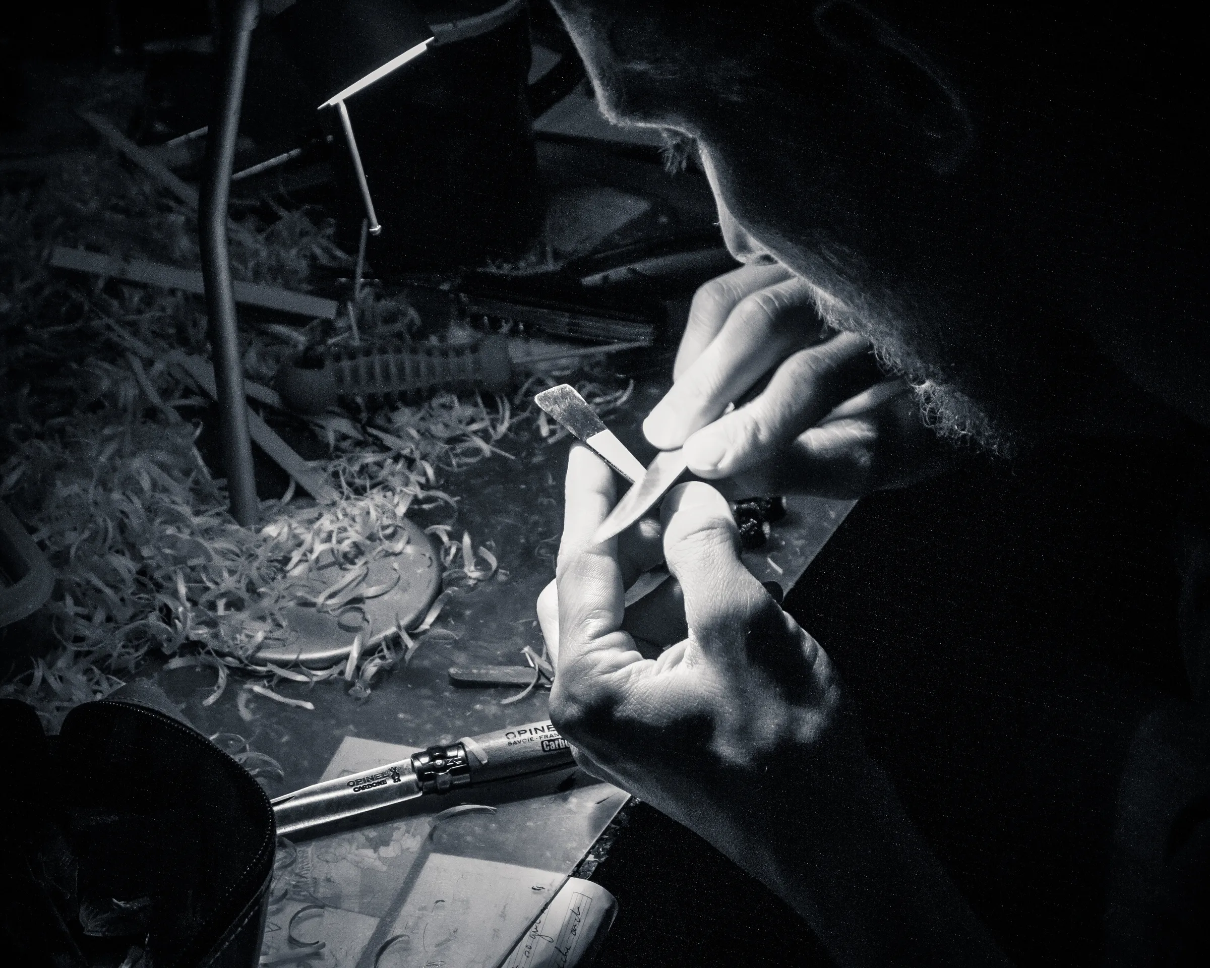 A pair of hands using a tool in a dimly lit workshop, with tools and debris on the floor.