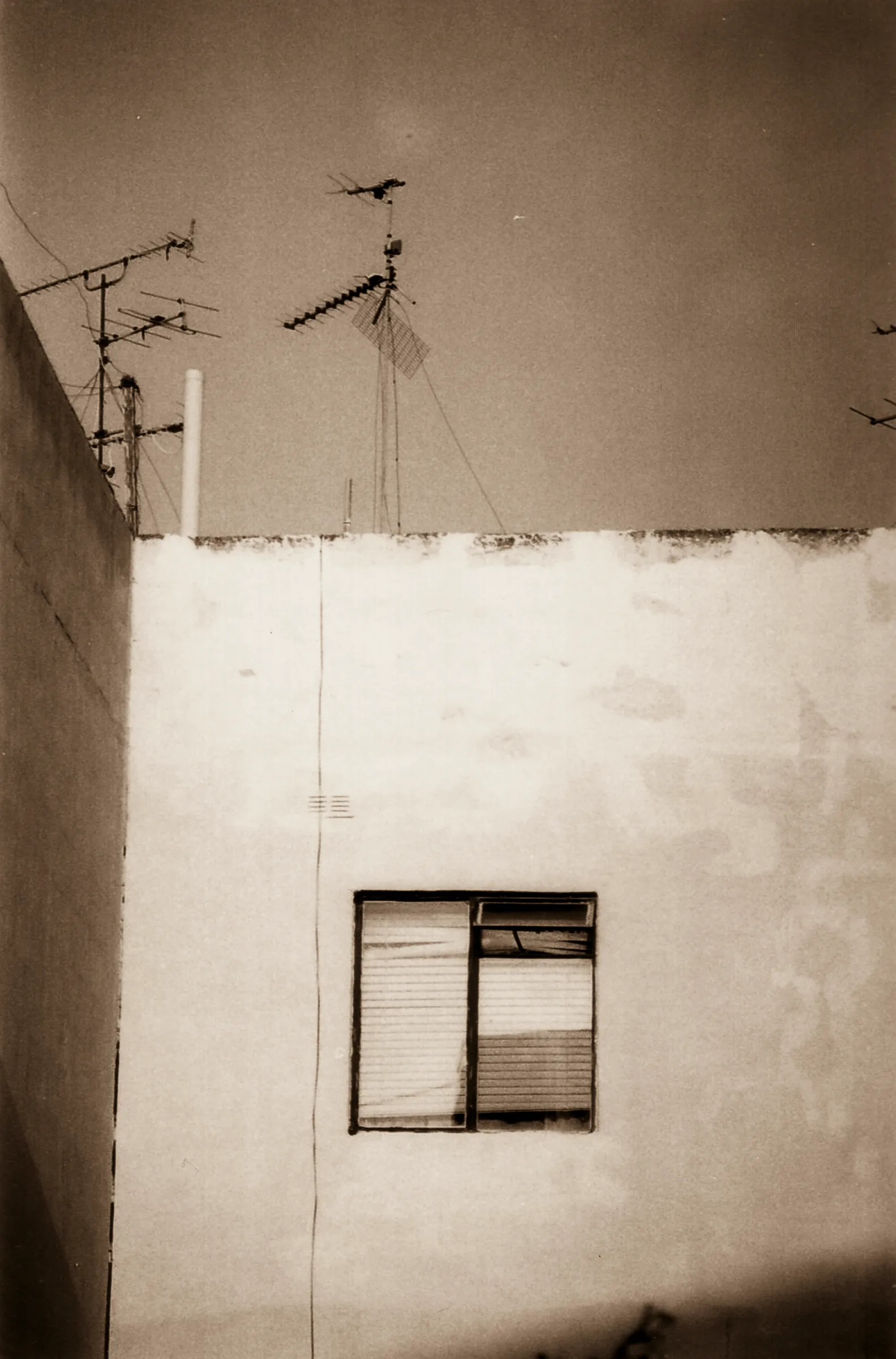 Building with two antennas on roof, single window below.