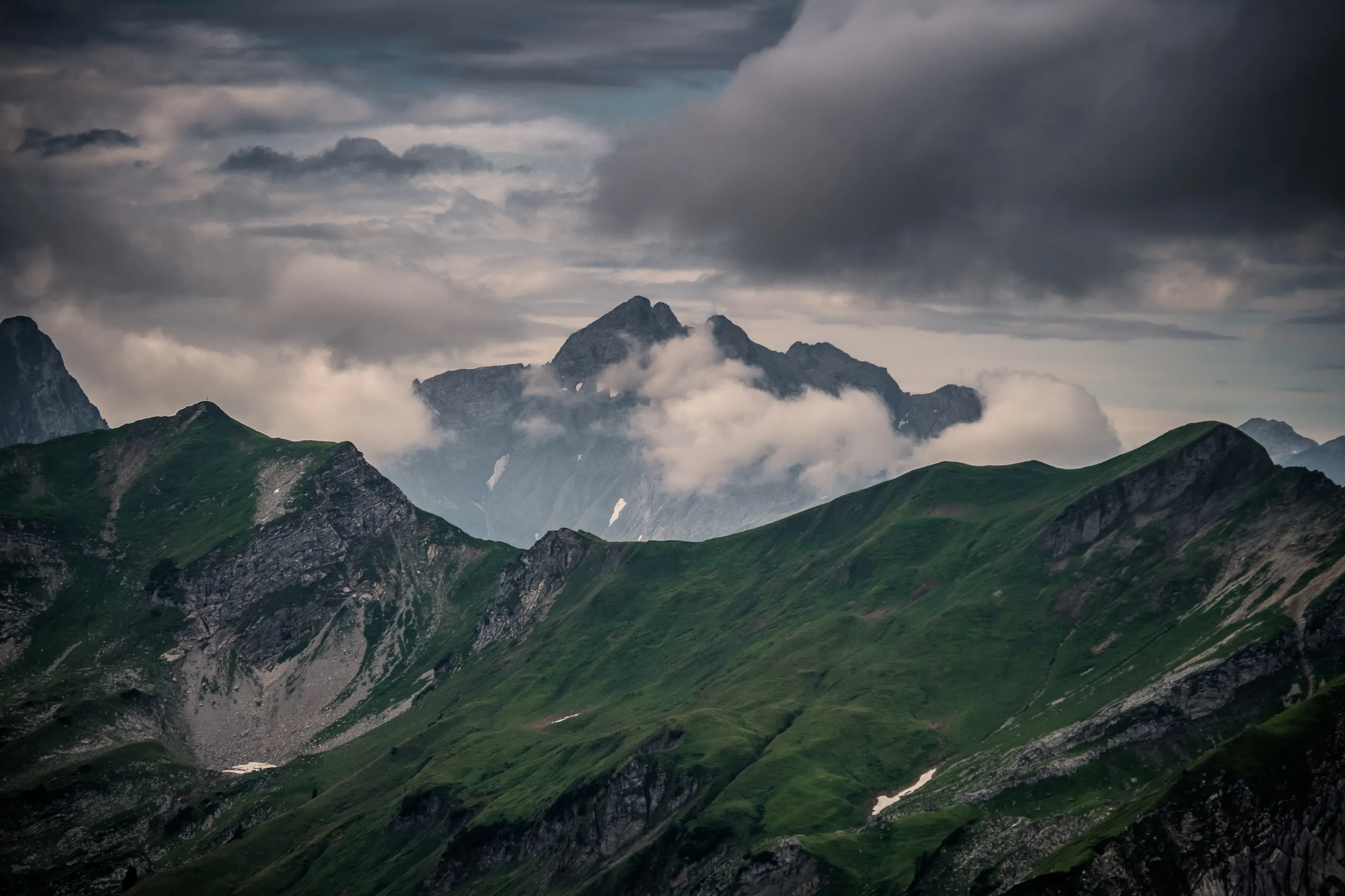 Mountains with peaks partially obscured by low-hanging clouds, surrounded by green valleys and rocky outcrops.