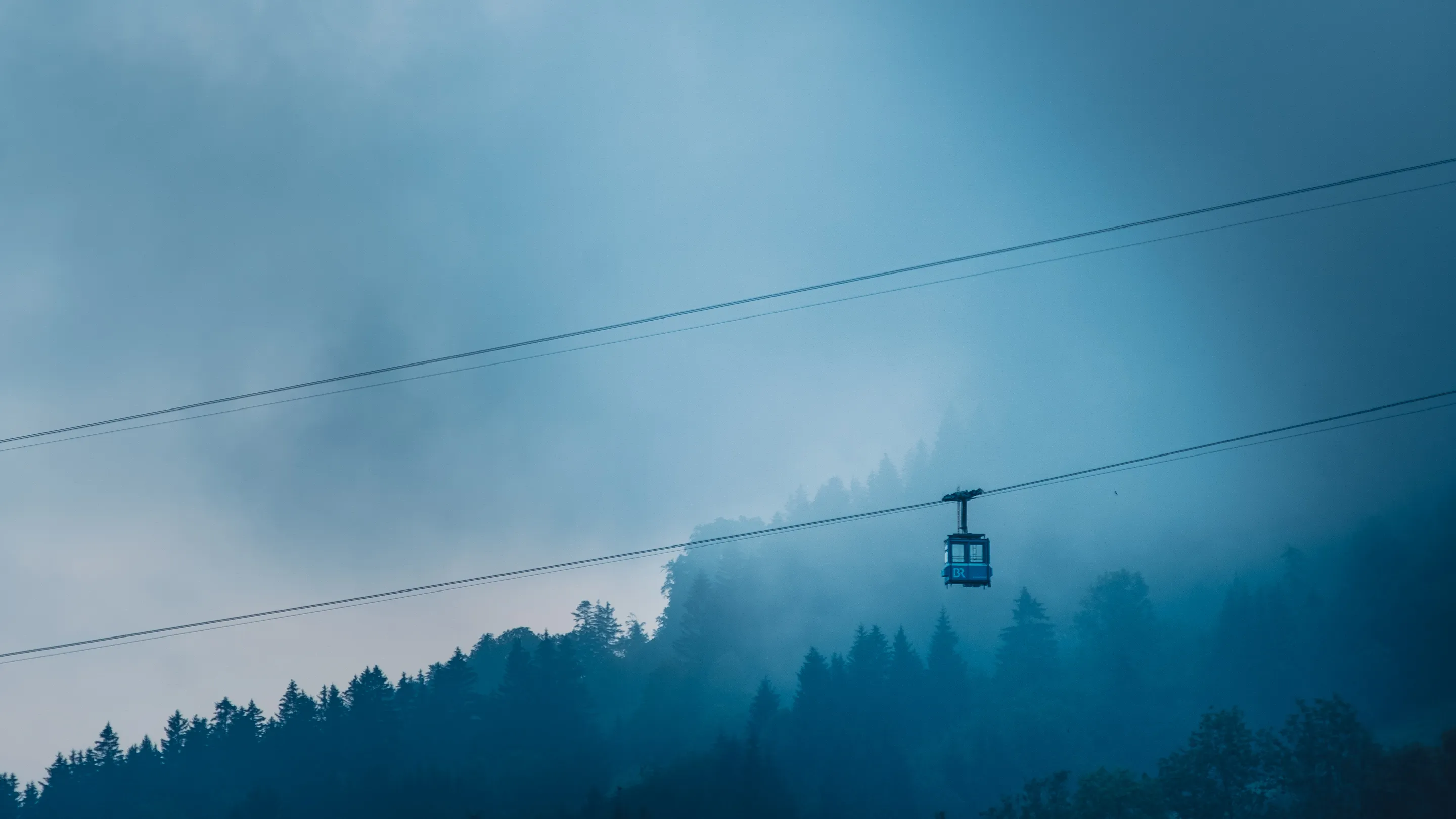 A cable car suspended above a misty forest, dark blue tones, minimalist landscape.
