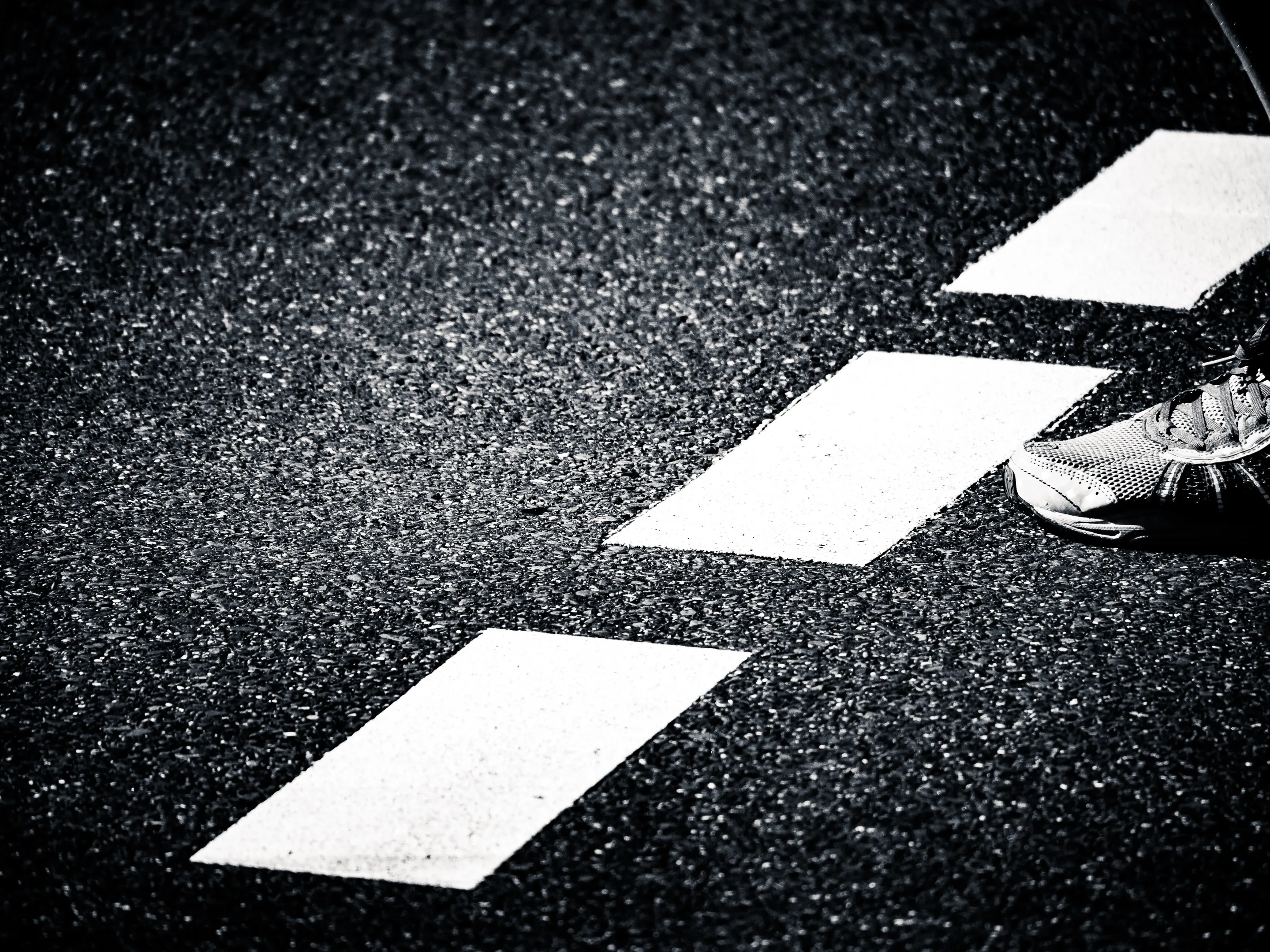 A foot stepping on white rectangular markings on a dark asphalt road, creating a zigzag pattern.