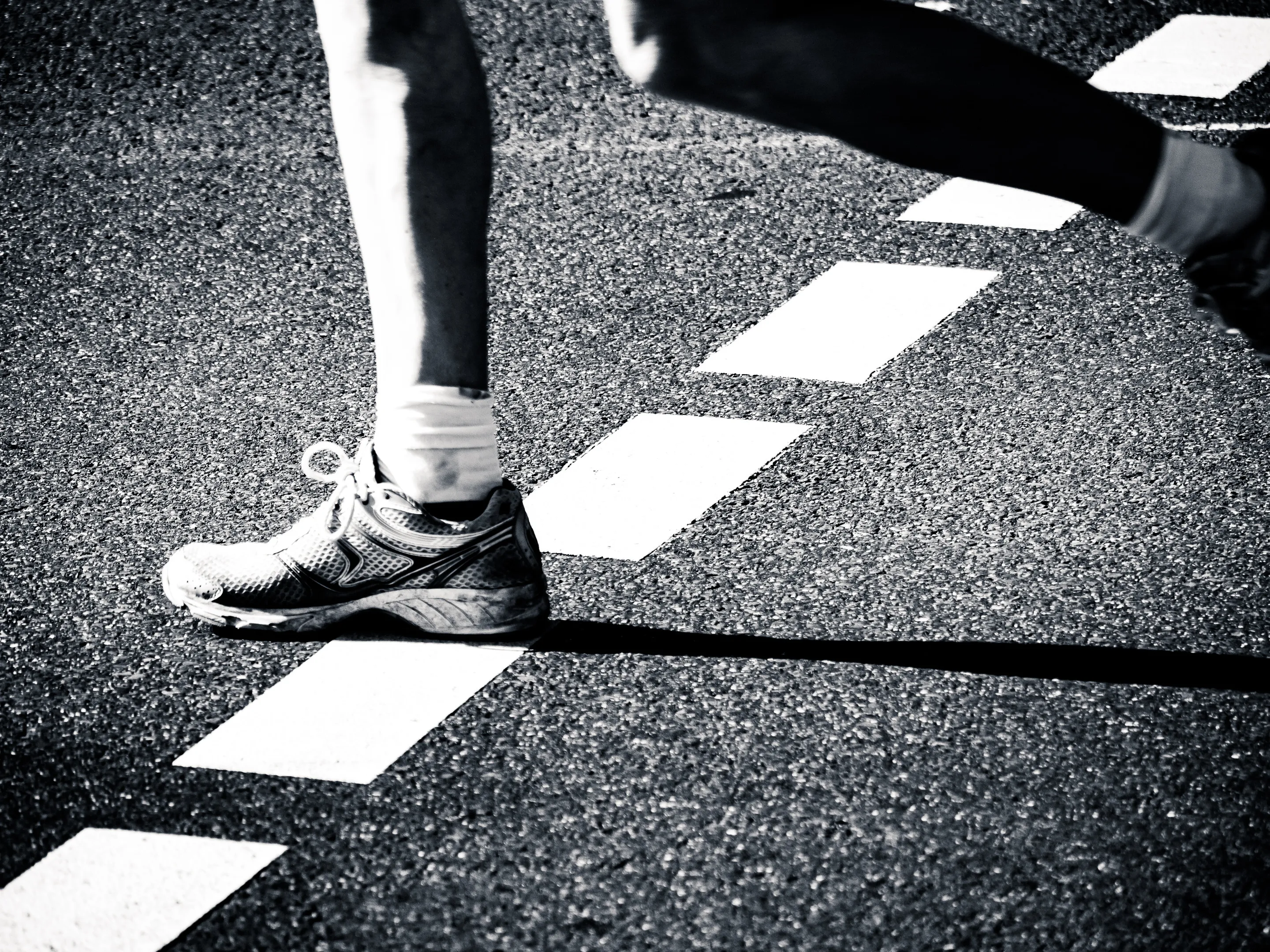 Feet in athletic shoes and socks stepping on white lines of a running track, black and white.