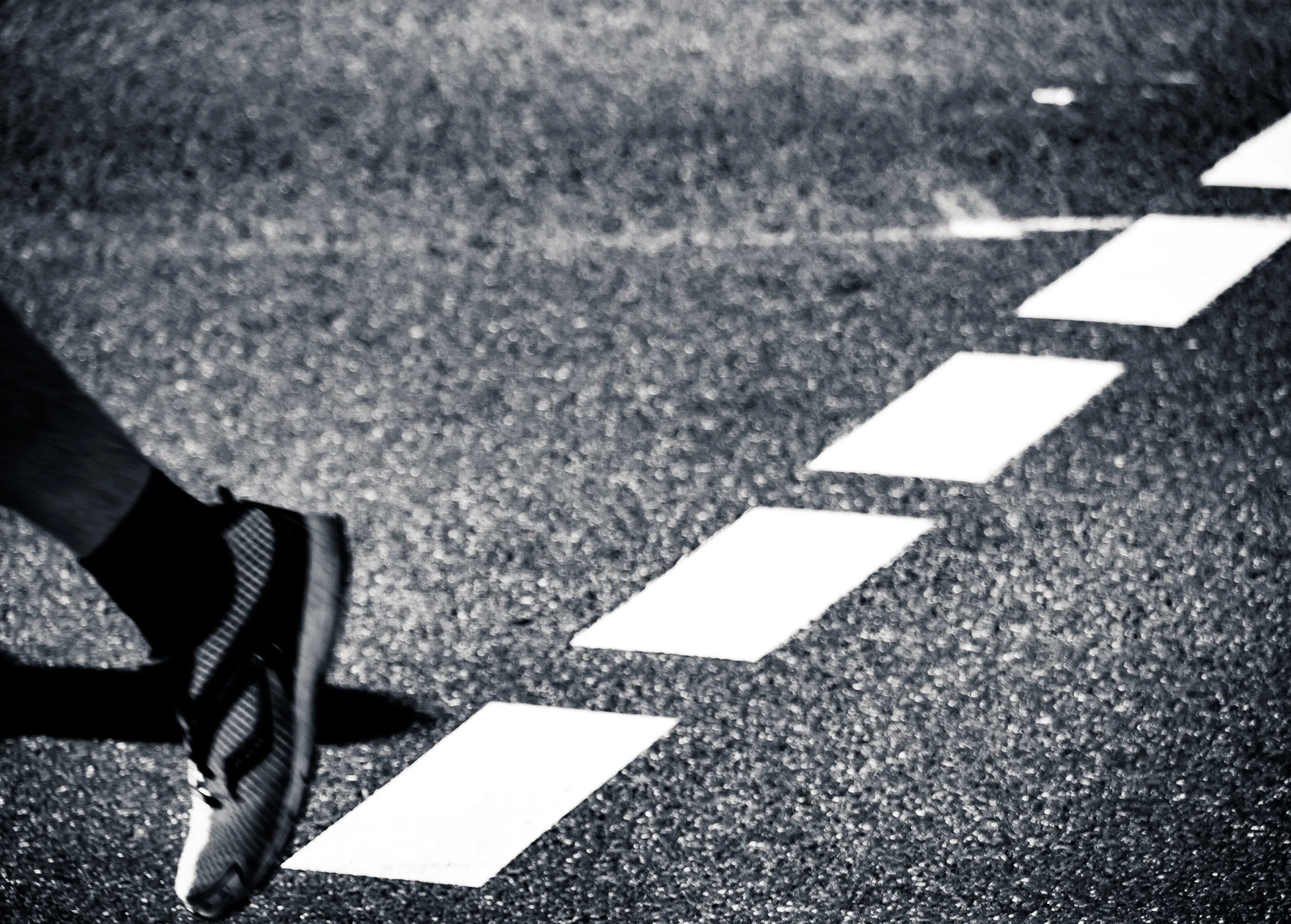 Person walking on a crosswalk, foot about to step on a white line.