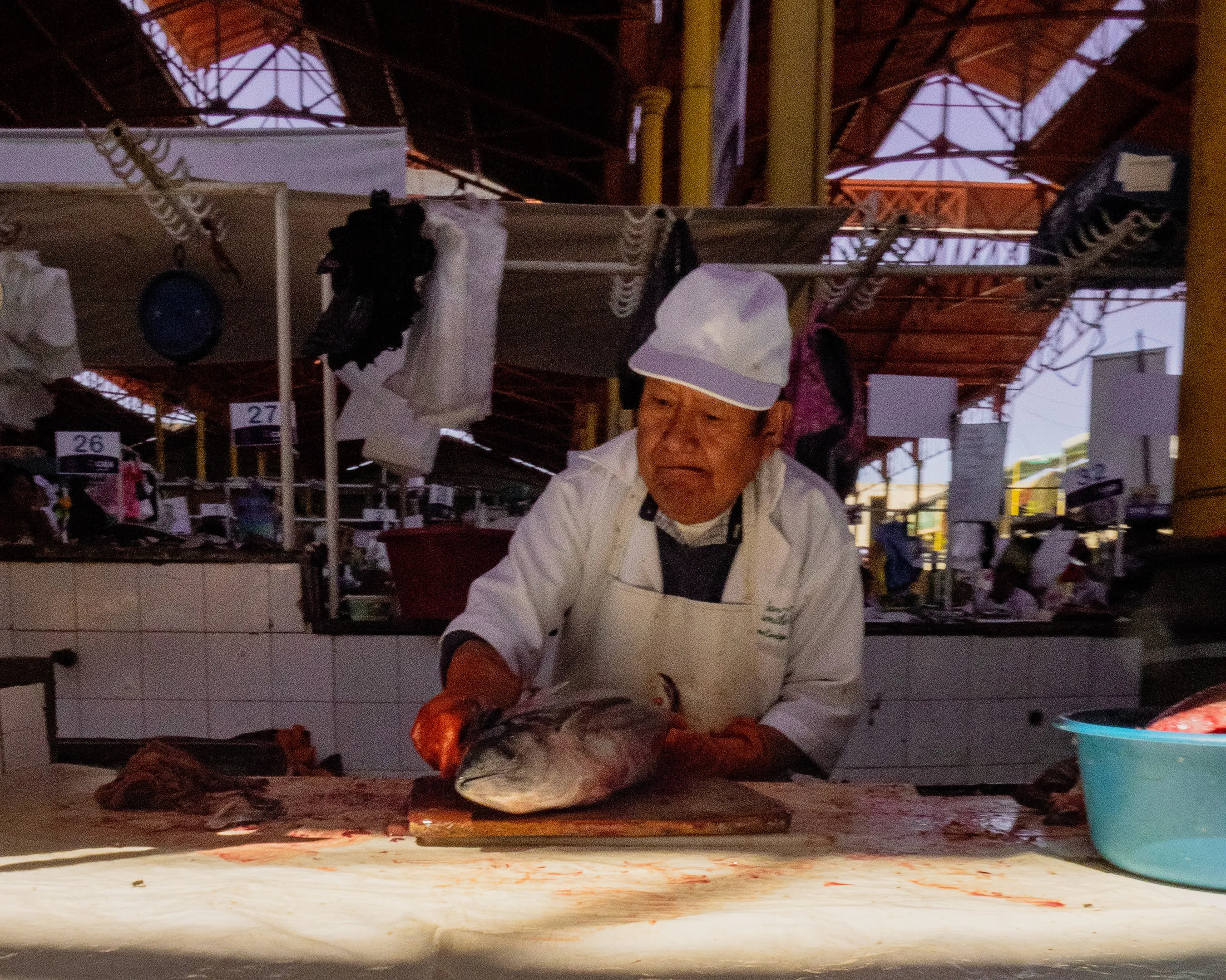Market worker in white cap and apron cleans fish on a wooden board.