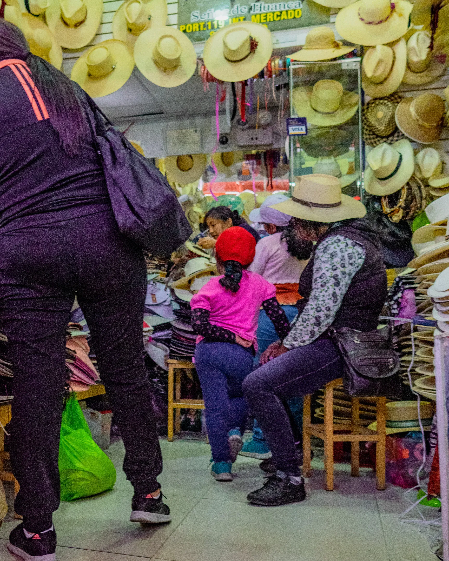 A bustling hat shop with hats on shelves and hanging from the ceiling, customers browsing and trying on hats.