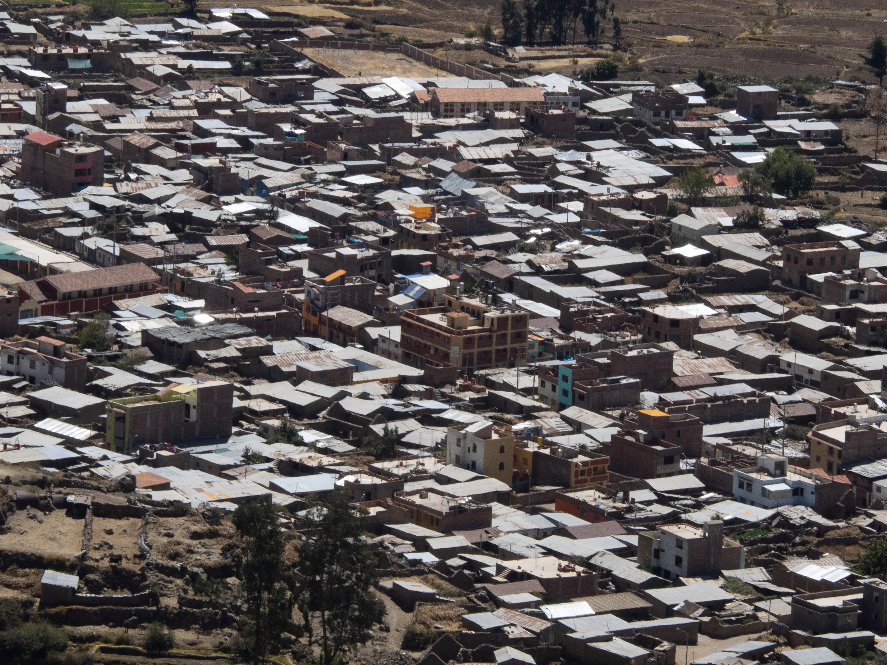 A densely packed slum area with numerous corrugated metal roofs, some buildings under construction, and sparse greenery.