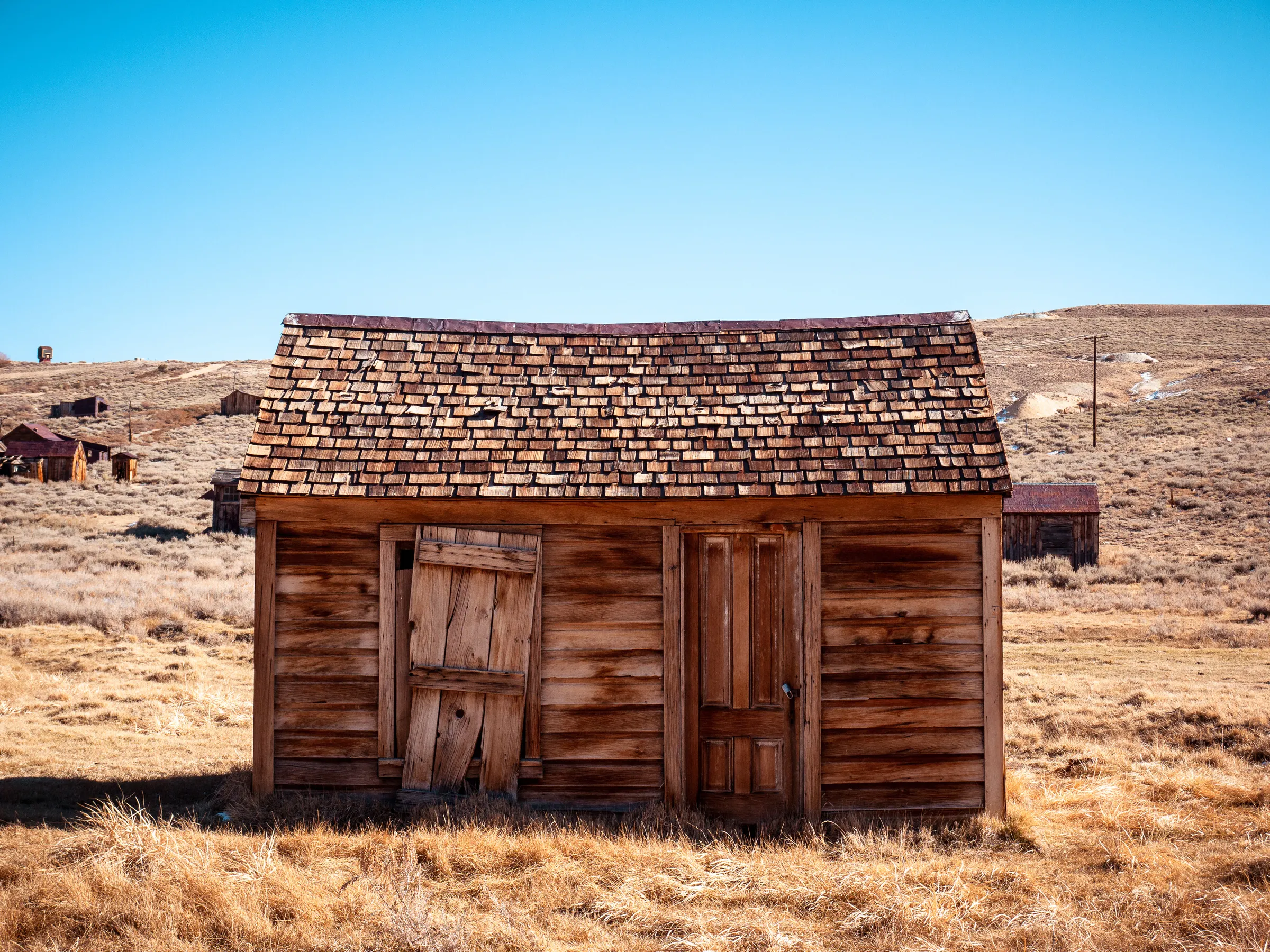 Abandoned wooden shed in arid landscape, rustic and weathered with a shingled roof.