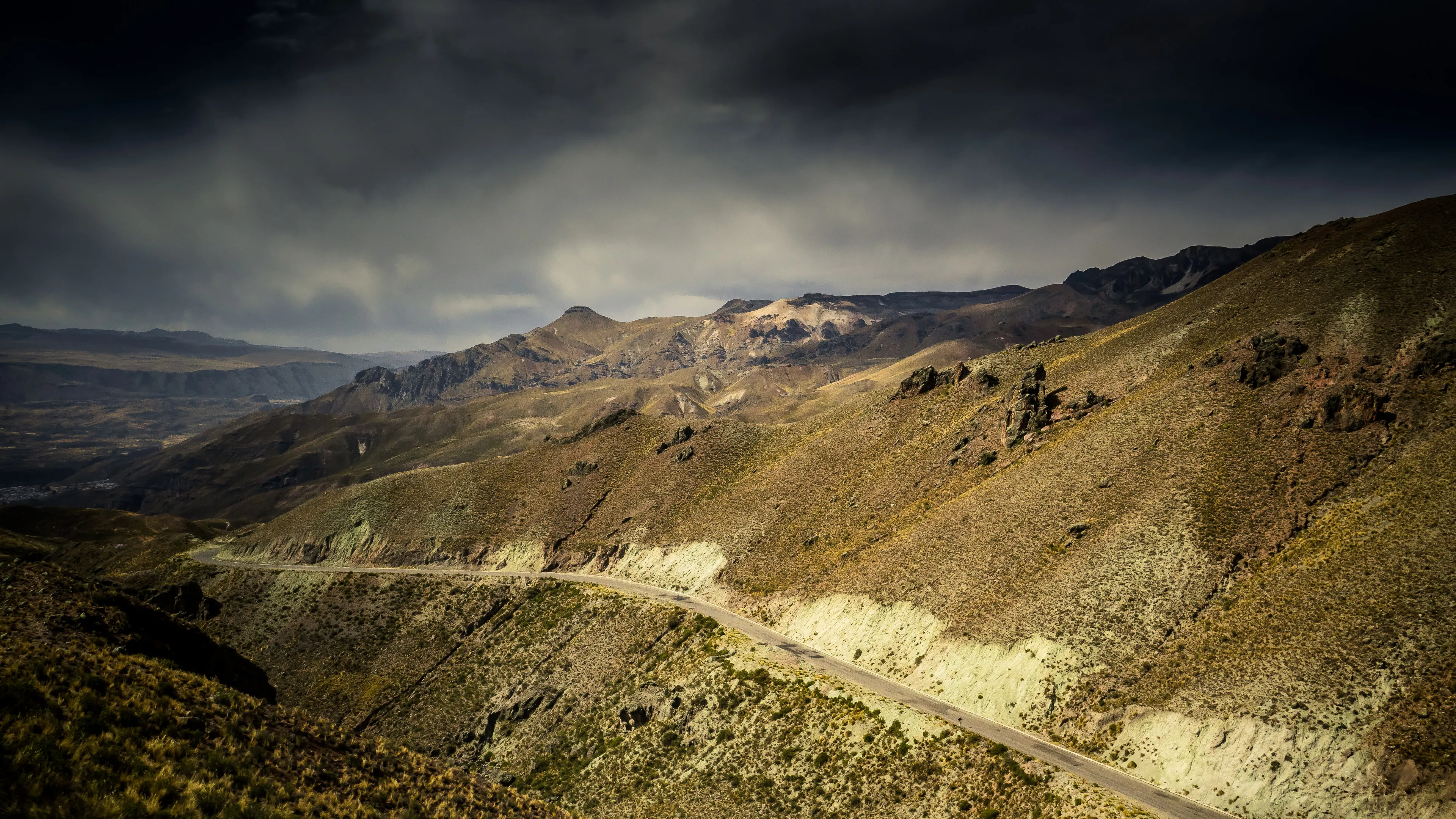 Winding road through hilly terrain under cloudy sky.