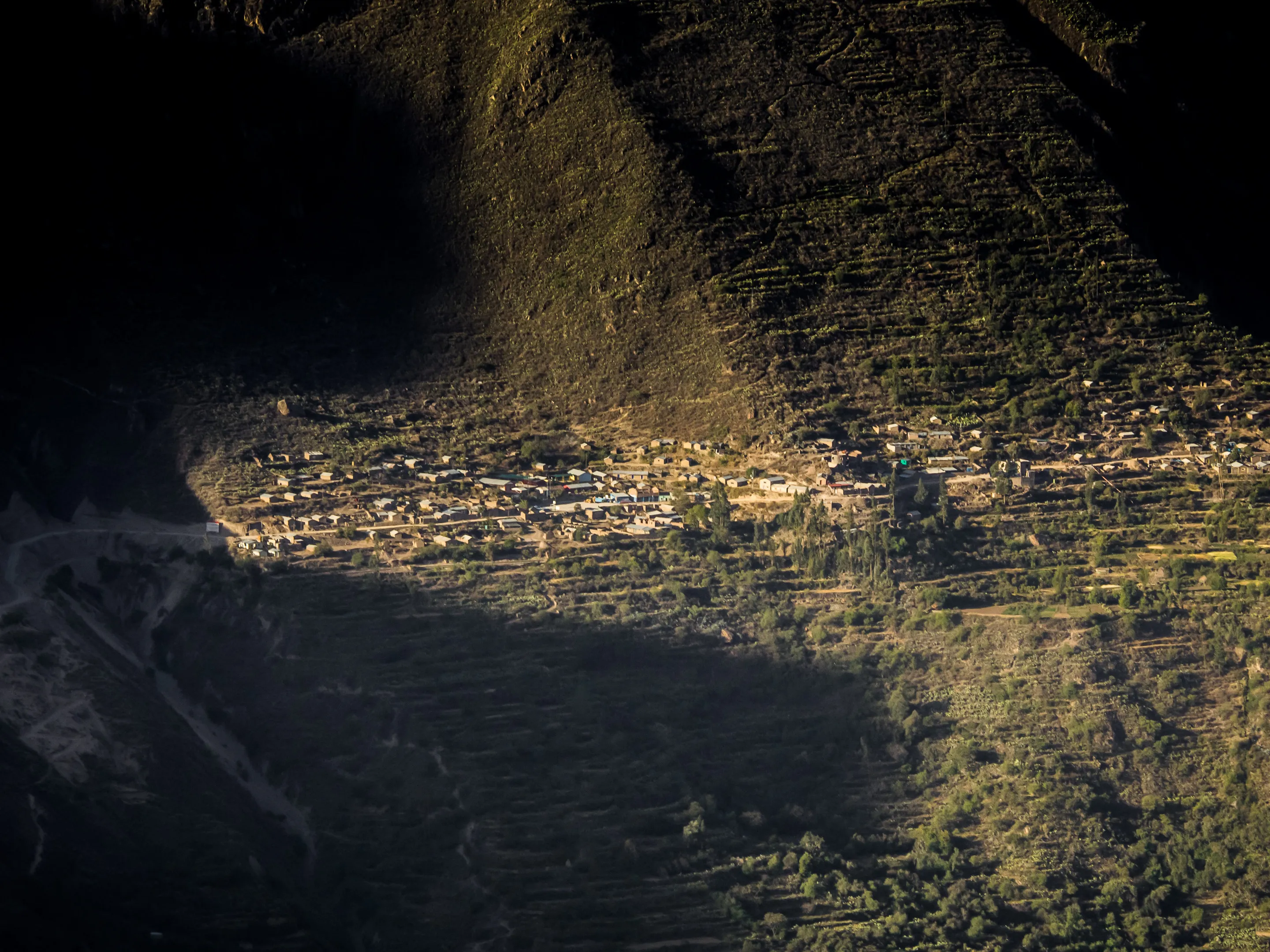 Aerial view of terraced fields at dusk, warm light on steps, dark silhouette of mountain in background.