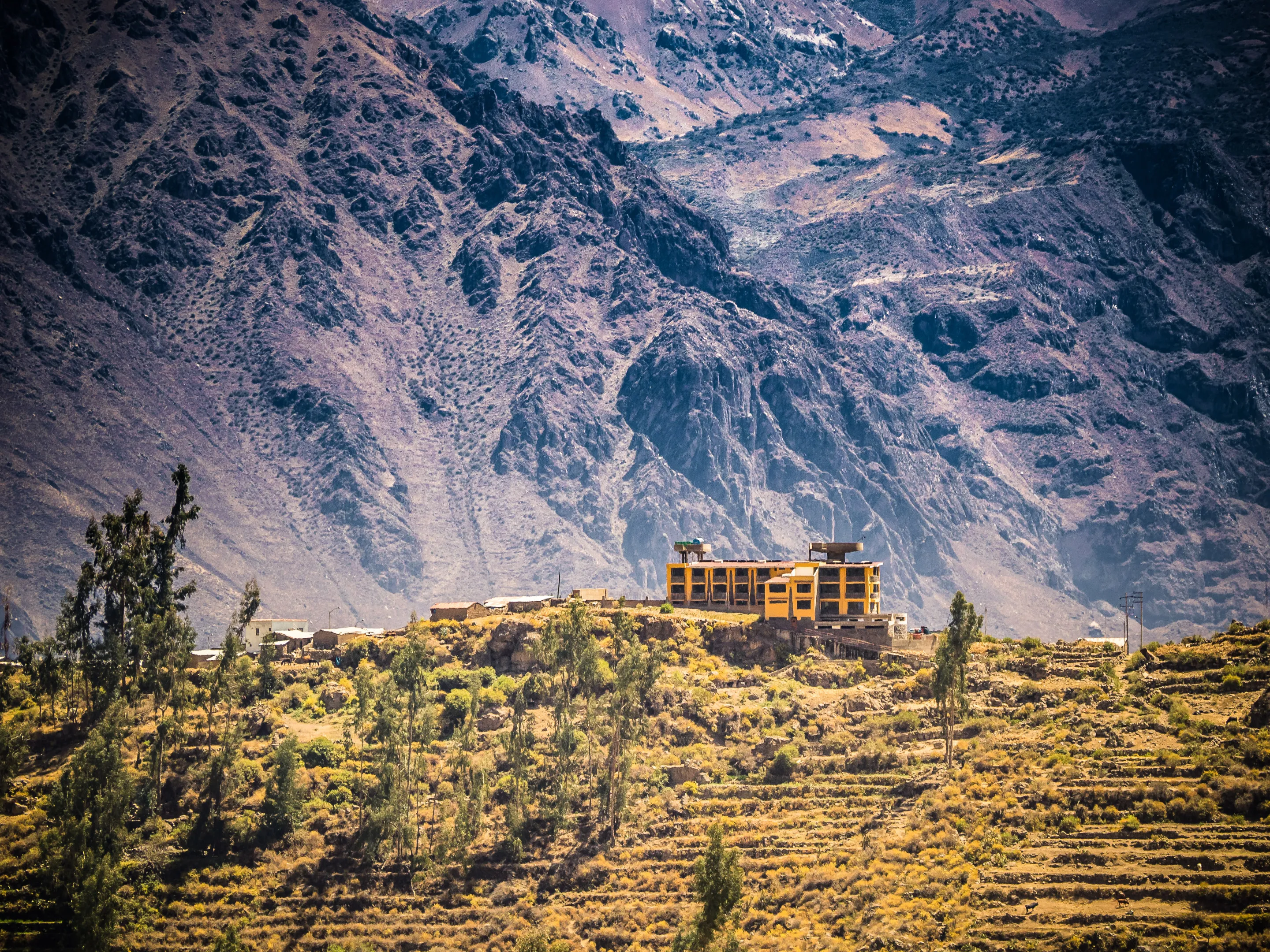 A large building nestled in a mountainous landscape with terraced fields.
