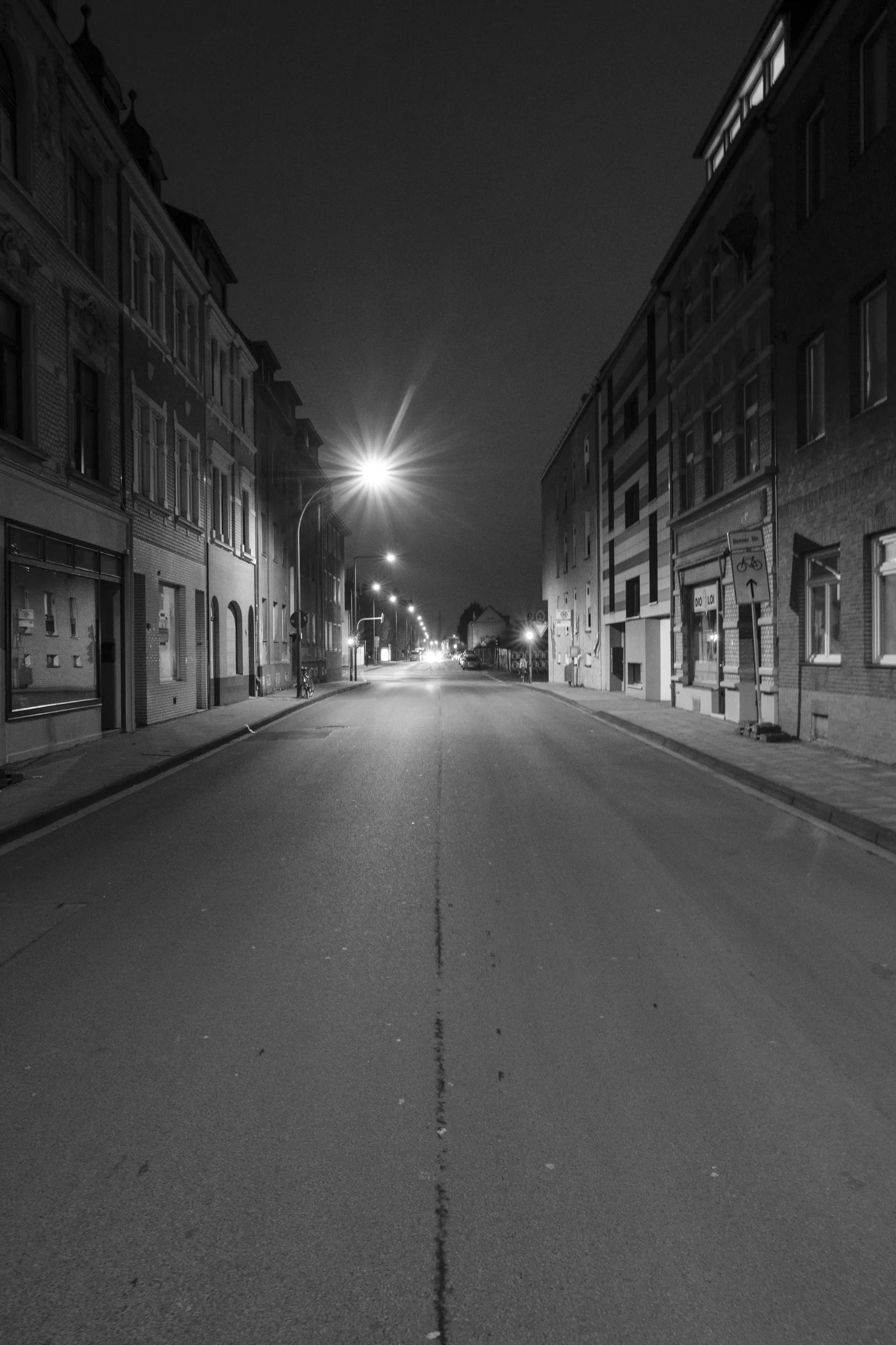 Empty street at night, lined with buildings, illuminated by a single streetlight.