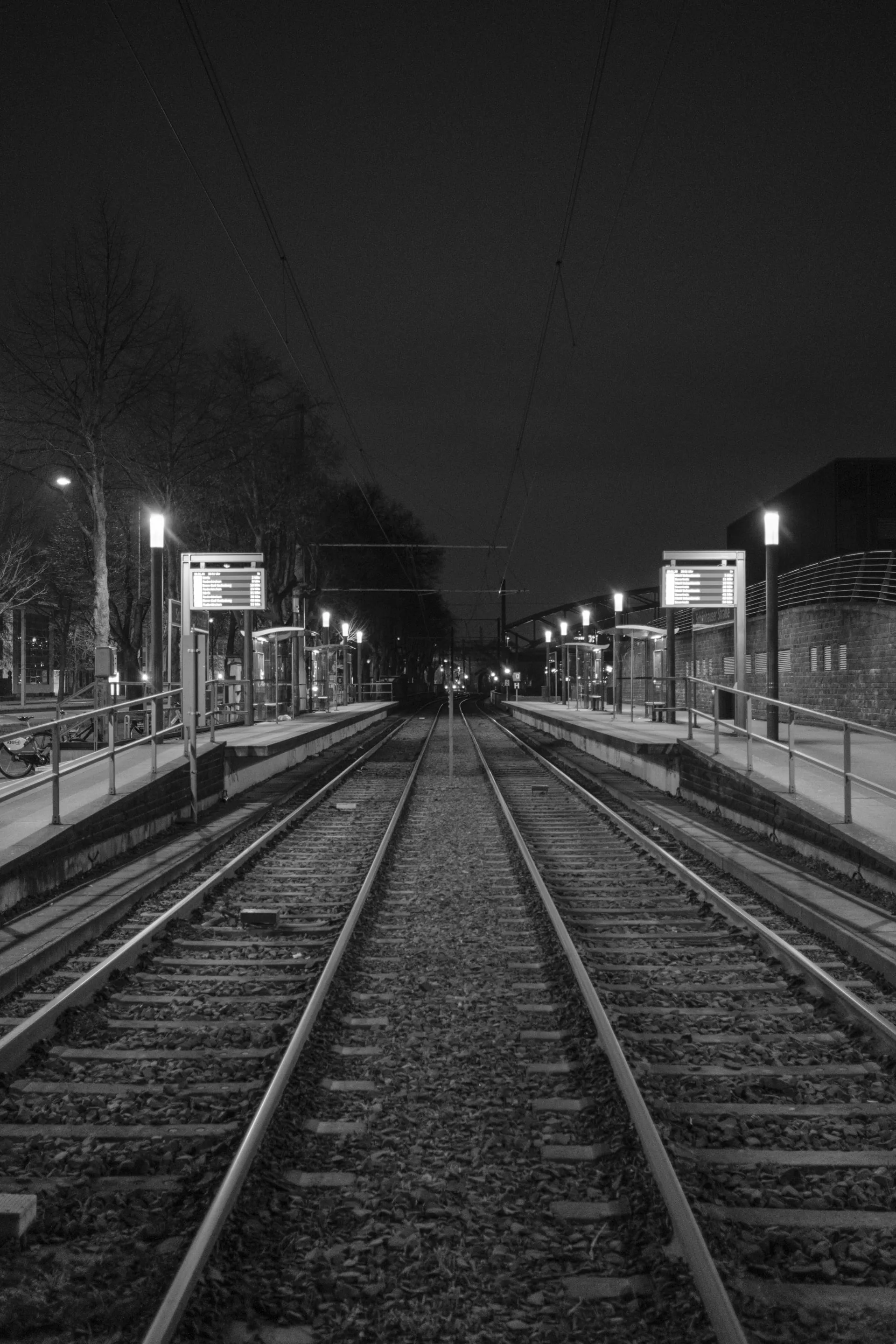Nighttime train station with empty tracks, lit platforms, and signage.