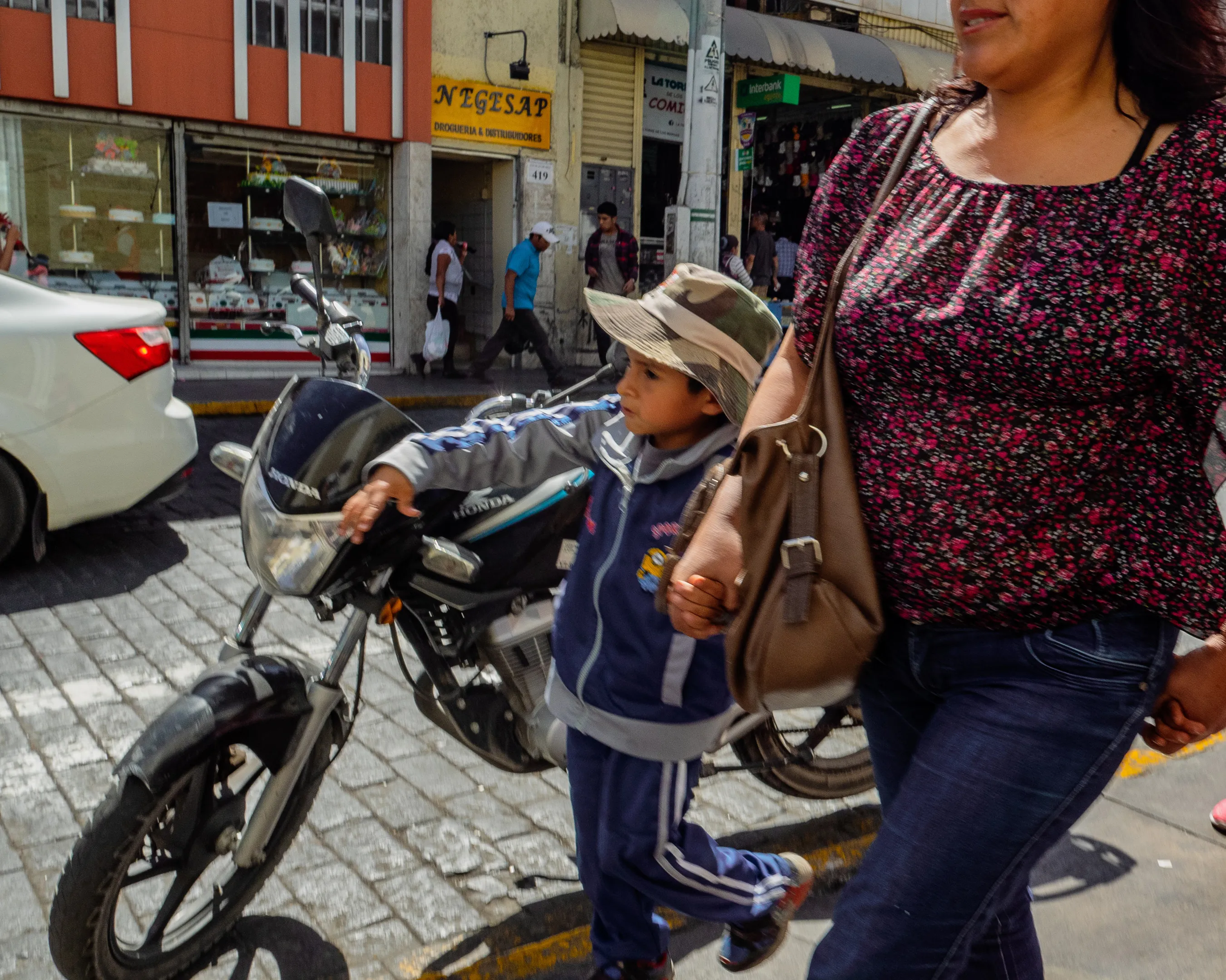 Woman with child holding hand, walking past motorcycle on busy street.