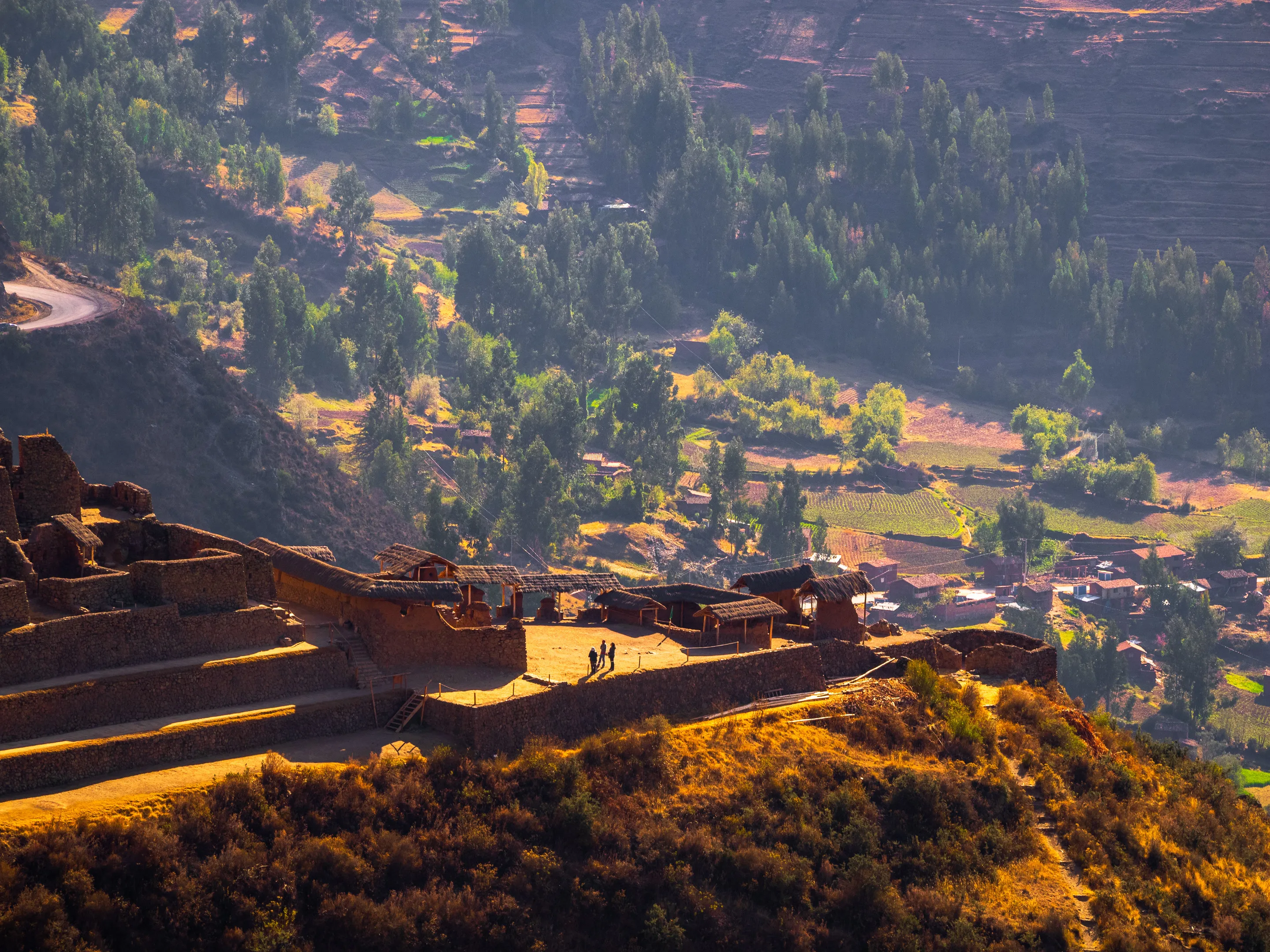 Mountainous landscape with terraced fields and a village nestled among trees, bathed in warm light.