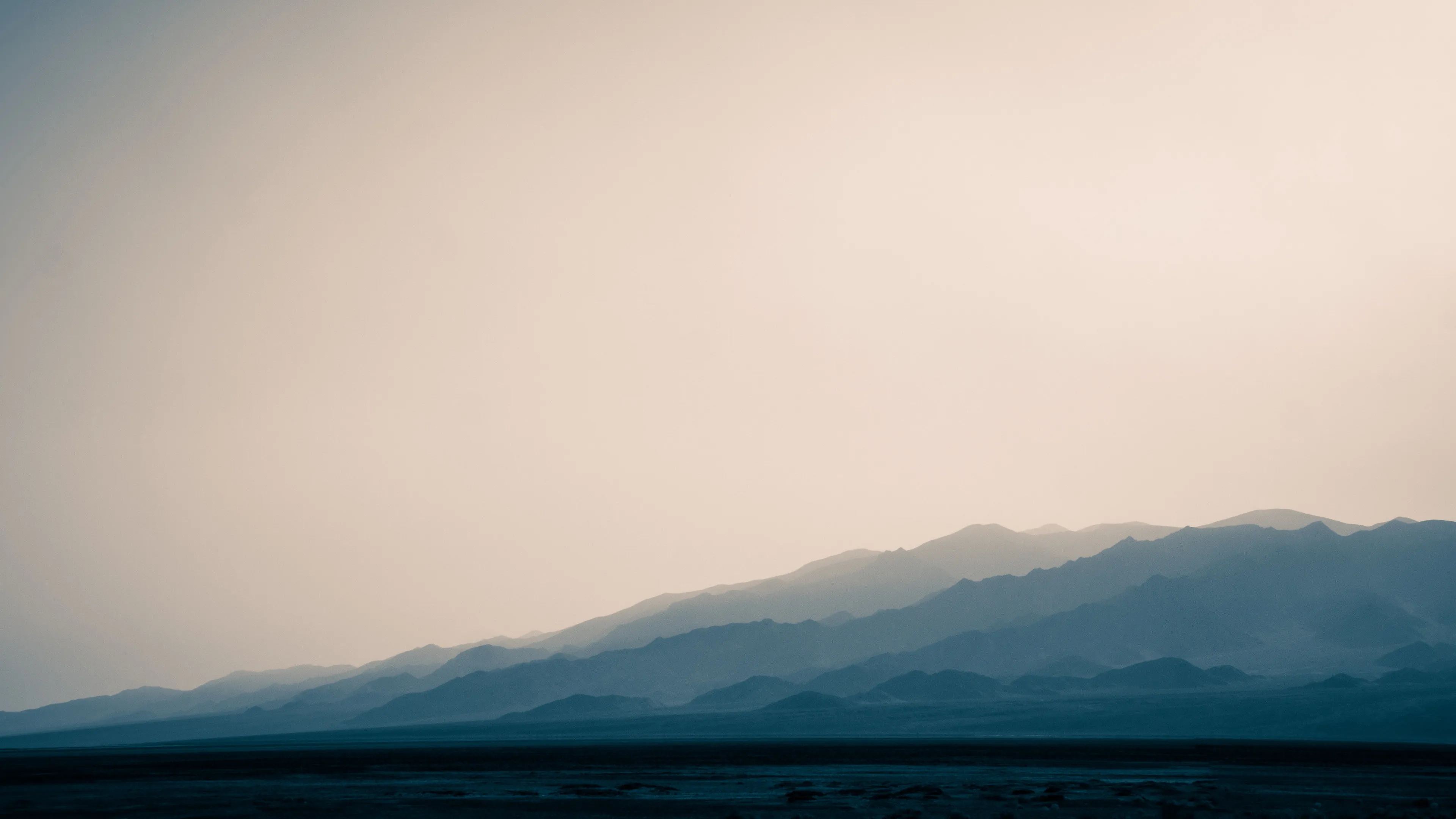Silhouetted mountains at dawn with soft gradient sky transitioning from blue to light orange, minimal landscape details visible.