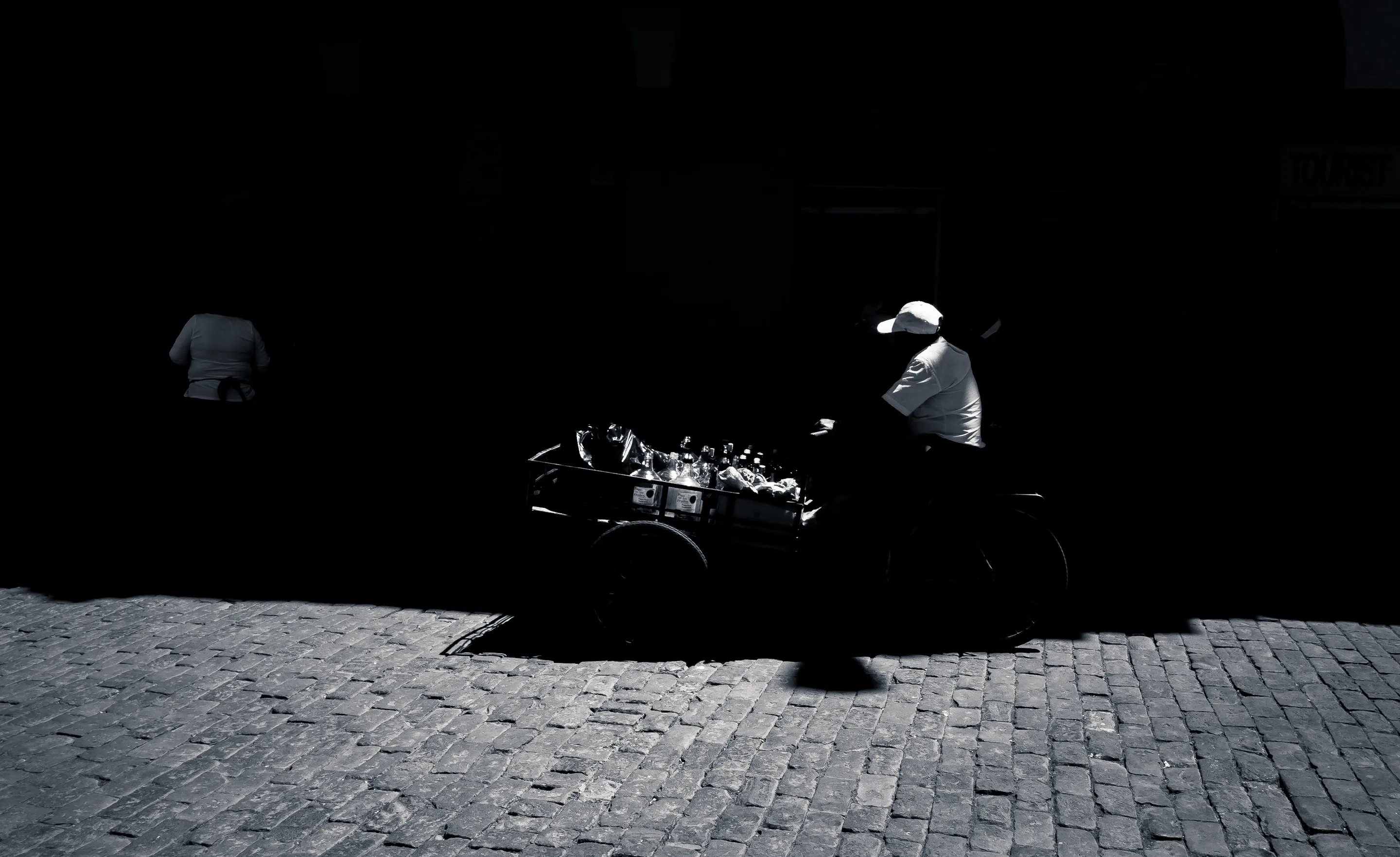 Silhouette of man riding a decorated motorcycle at night on brick road, another figure walking in background.