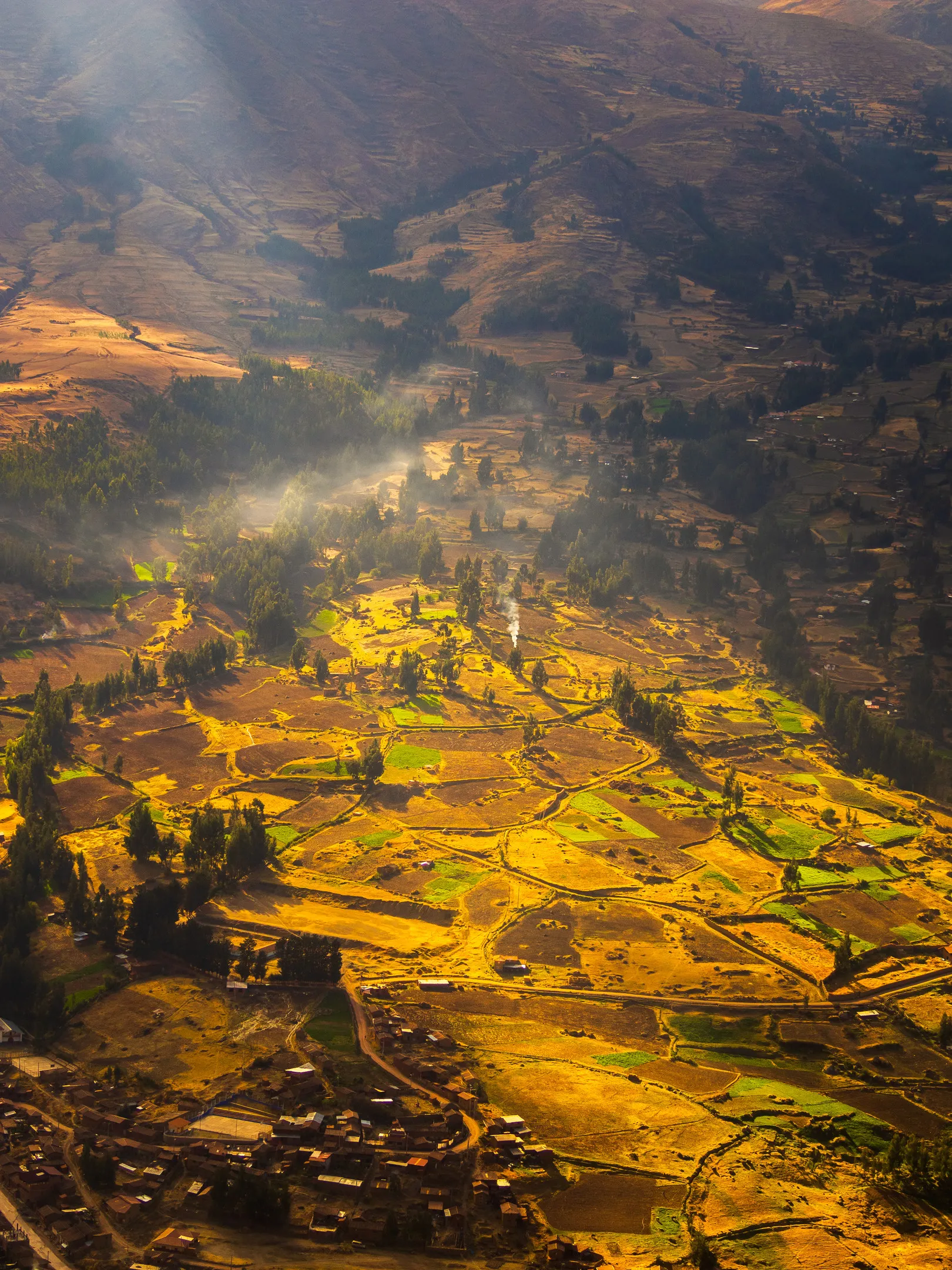 Aerial view of terraced fields in a valley, with morning mist and sunlight highlighting the landscape.