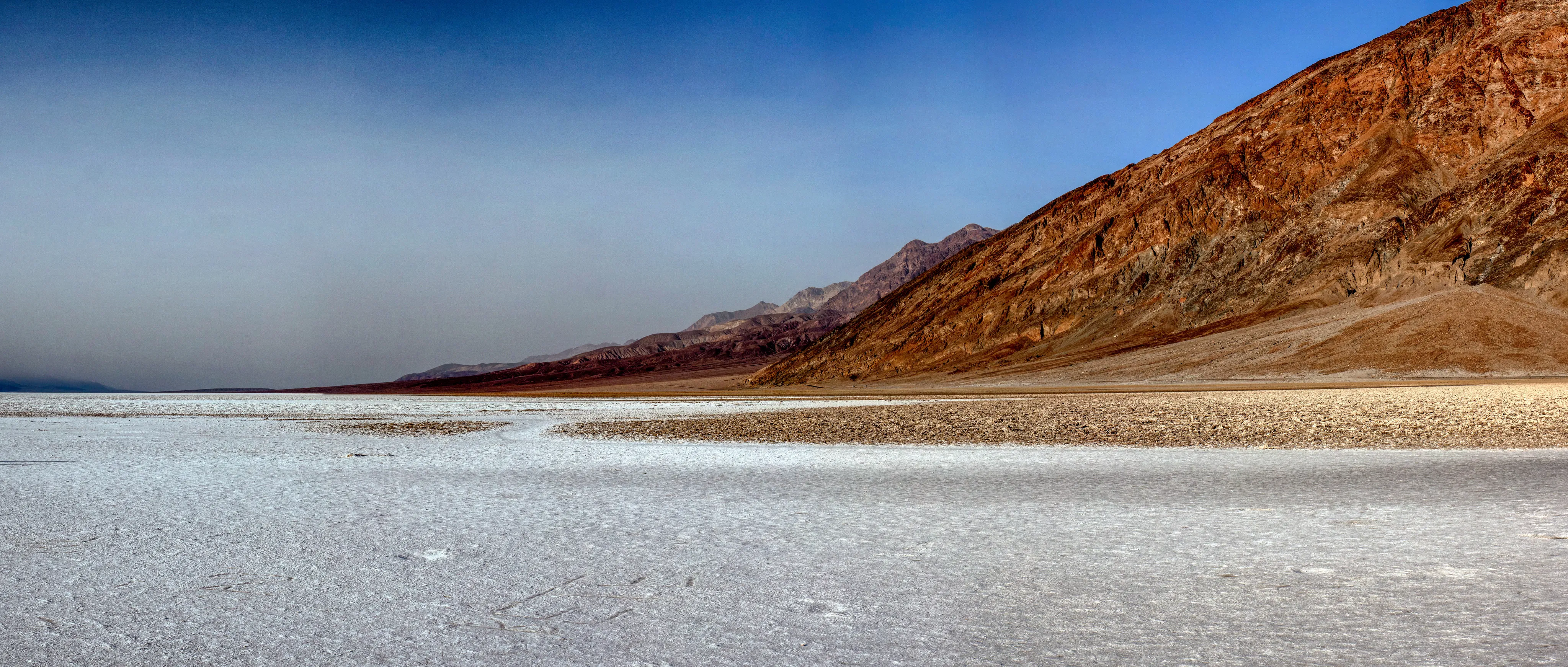 Desert landscape with salt flats and distant red mountains under a blue sky.